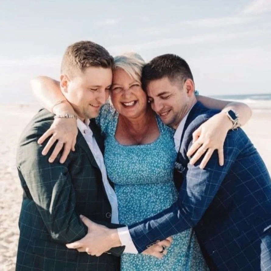 Upbeat wedding celebrant hugging two grooms during LGBTQI+ ceremony