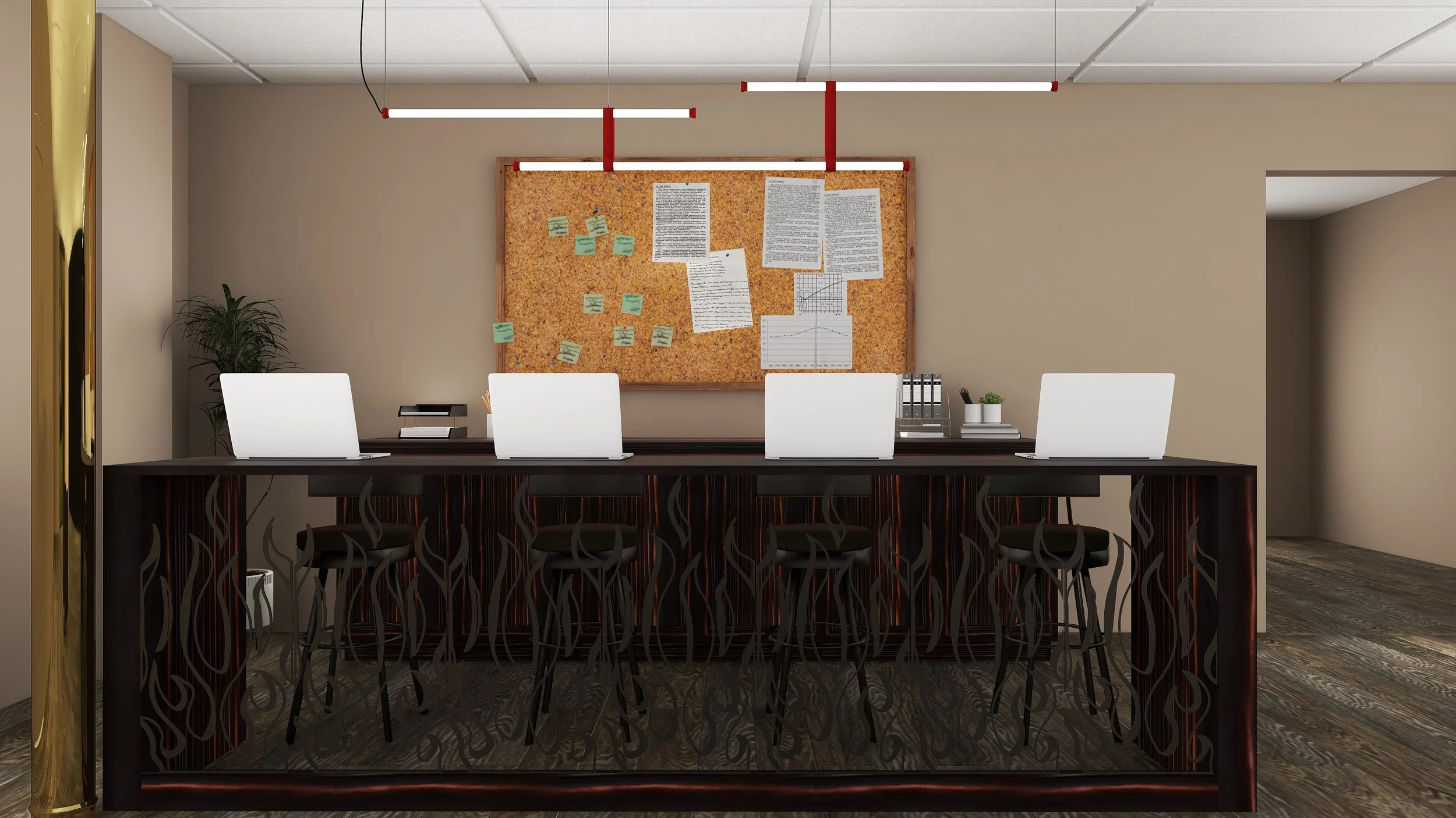 An office workspace with a long black desk, four white laptops, a potted plant, some files, and a cork bulletin board with papers and sticky notes. Four black chairs are neatly tucked under the desk. Overhead lighting fixtures hang from the ceiling.