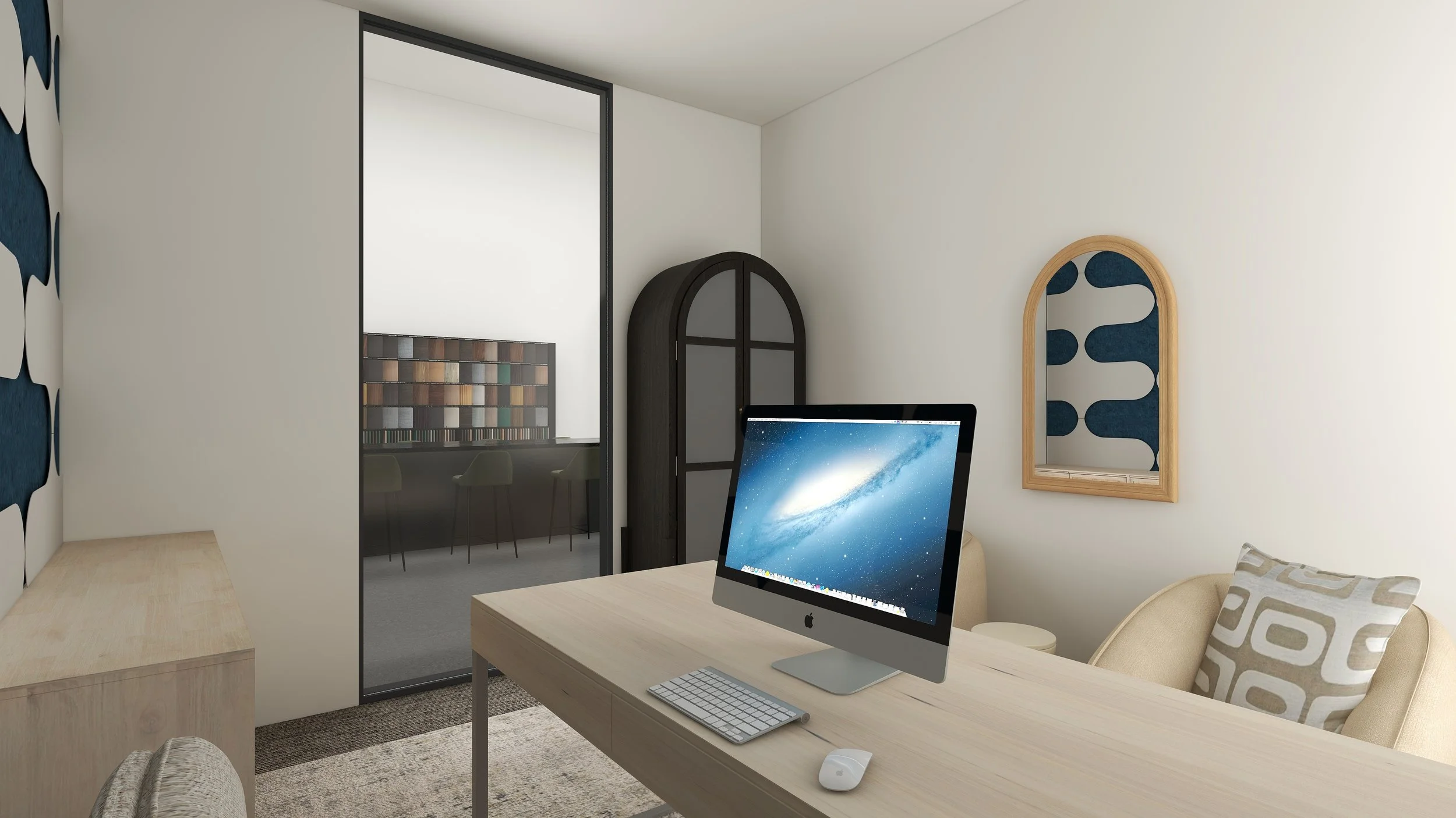 A workspace with a wooden desk holding an iMac computer, a keyboard, and a mouse. Behind the desk is a beige couch with patterned pillows. The wall features a wooden-framed mirror with a blue design inside. To the left, there is a partial view of a r