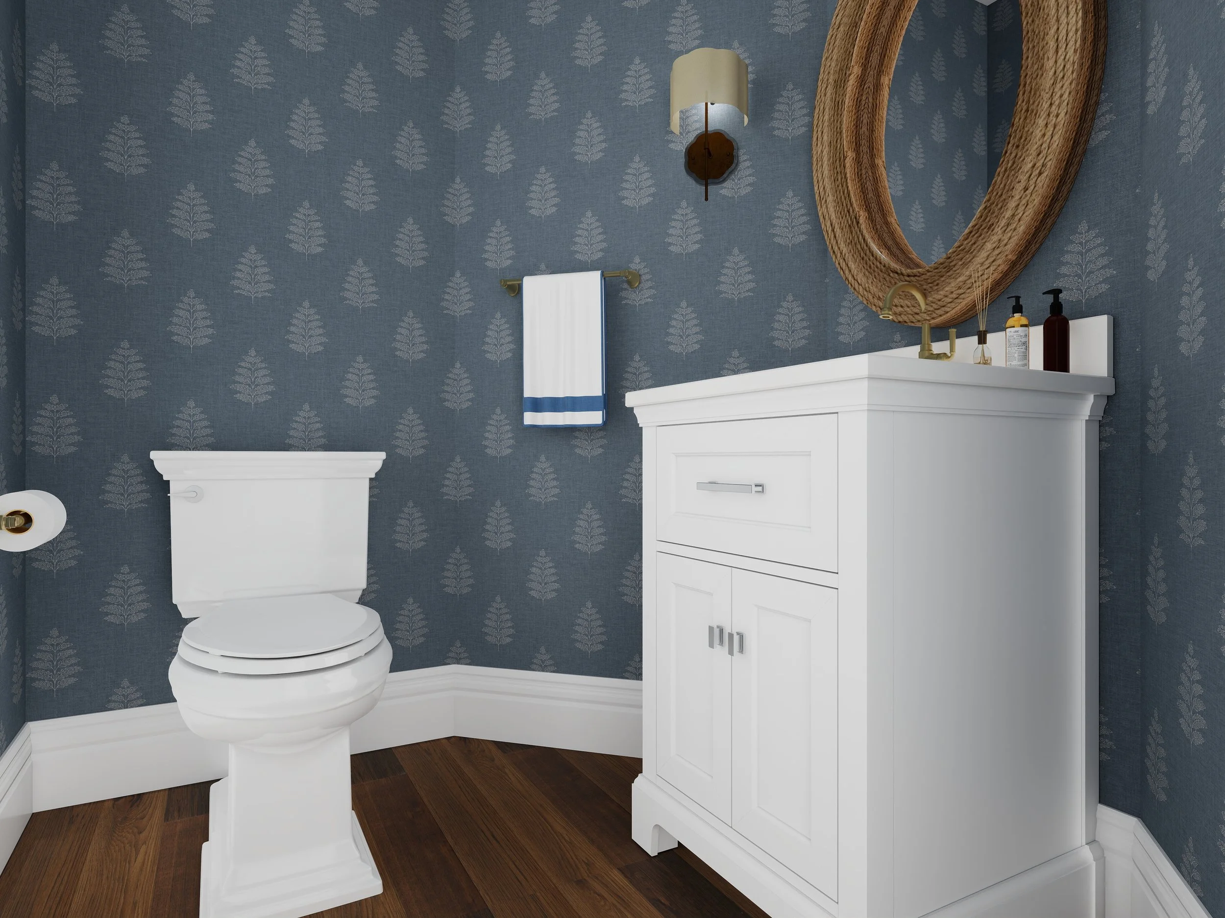 A bathroom with blue wallpaper featuring a pattern of white leaves, white toilet with a gold flush handle, wall-mounted light fixture with a beige shade, white vanity cabinet with a mirror that has a woven wooden frame, and several bottles on top of 