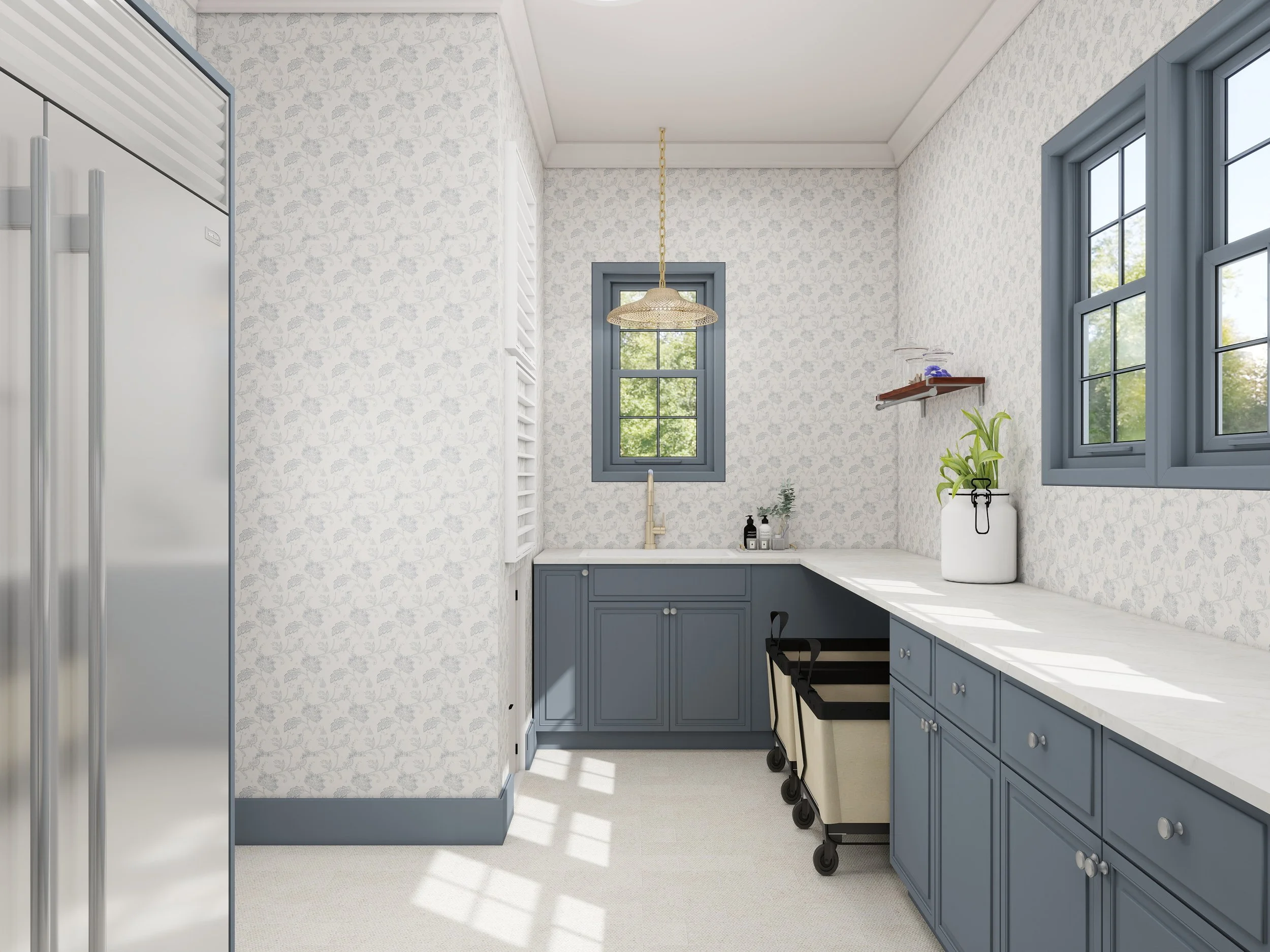 A bright kitchen with white floral wallpaper, blue cabinets, and two small windows showing green trees outside. There is a hanging light fixture above a white countertop.