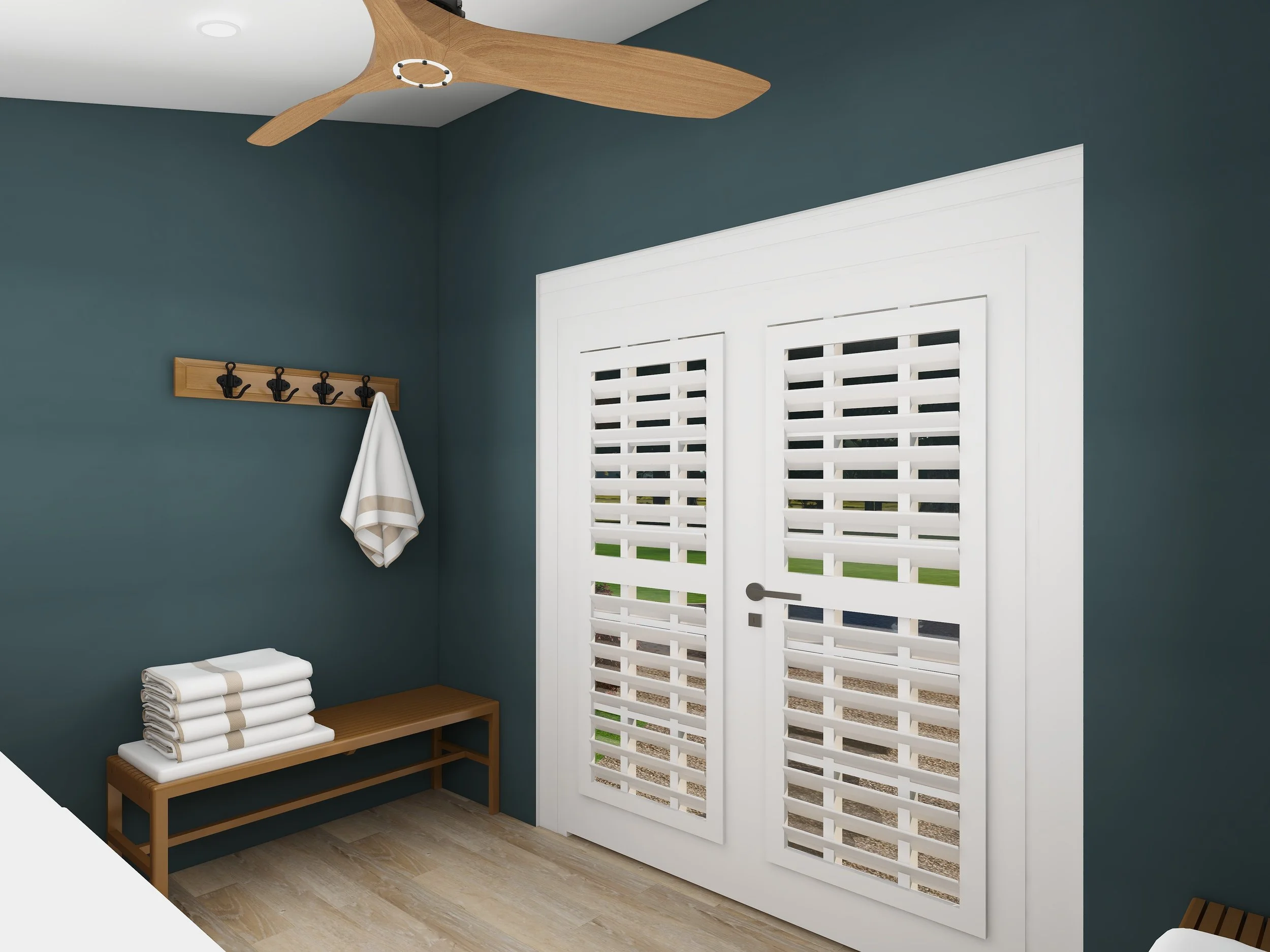 A room with dark teal walls, a white door with window slats, a wooden bench with folded white towels, a wooden coat rack with black hooks, and a ceiling fan with wooden blades.