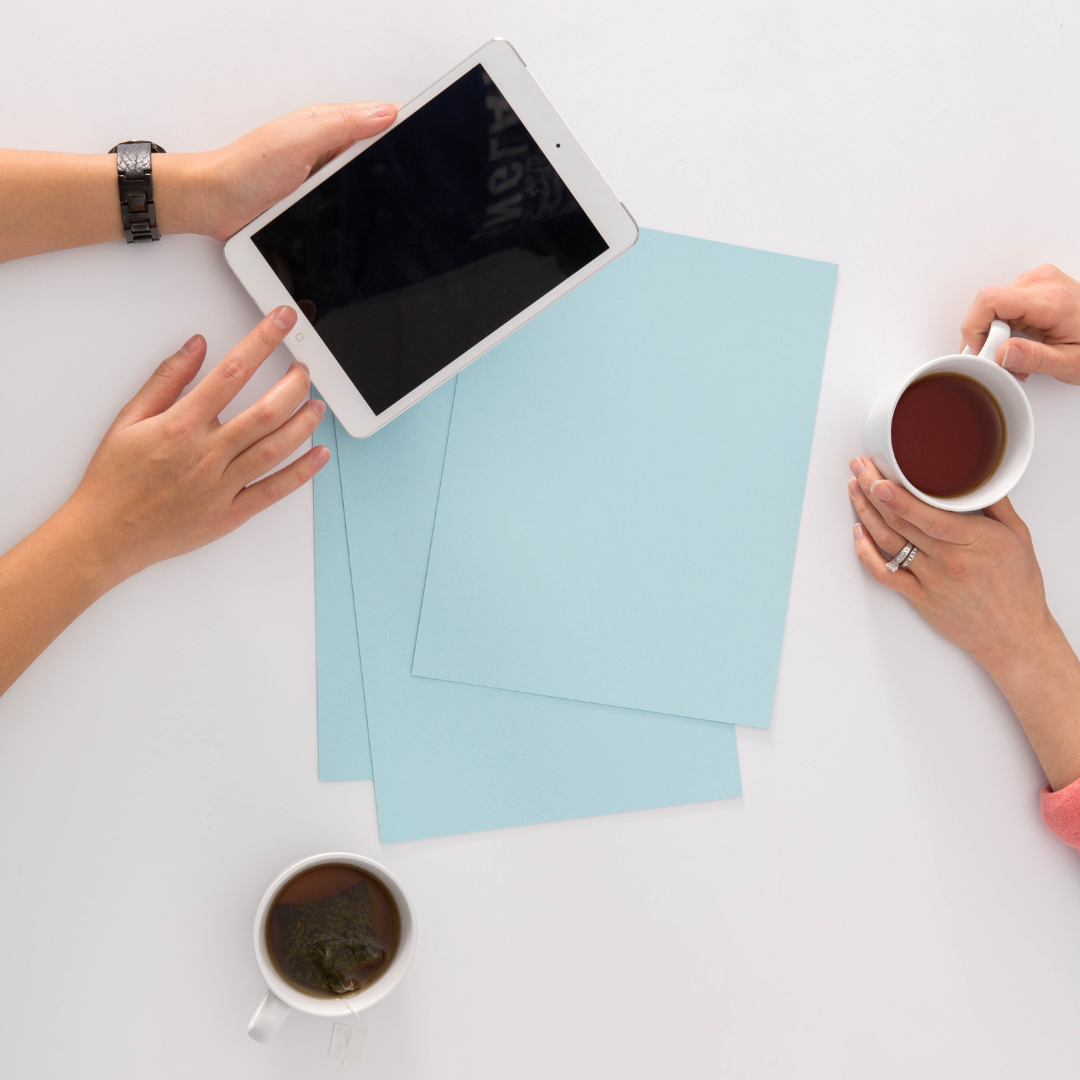 Top view of two people at a table with blue papers, a tablet, and two cups of tea.