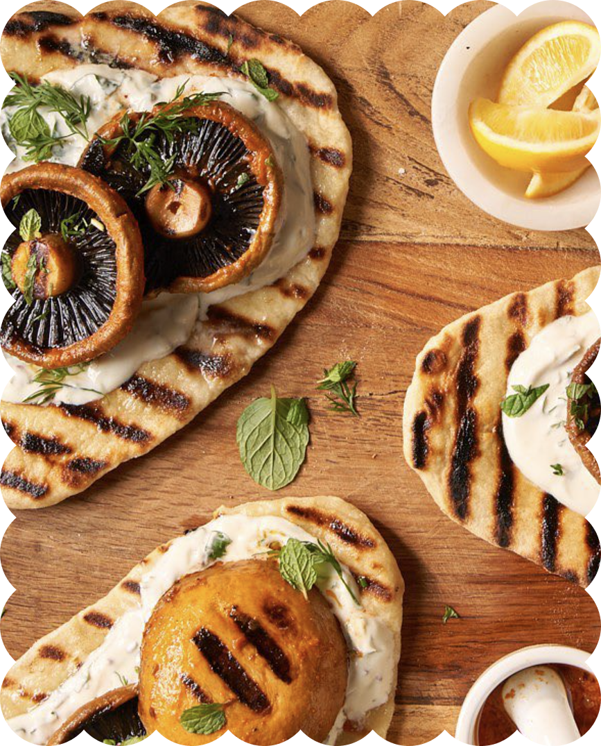 Grilled flatbread pizza topped with mushrooms, cheese, and herbs, served with lemon wedges and dips.