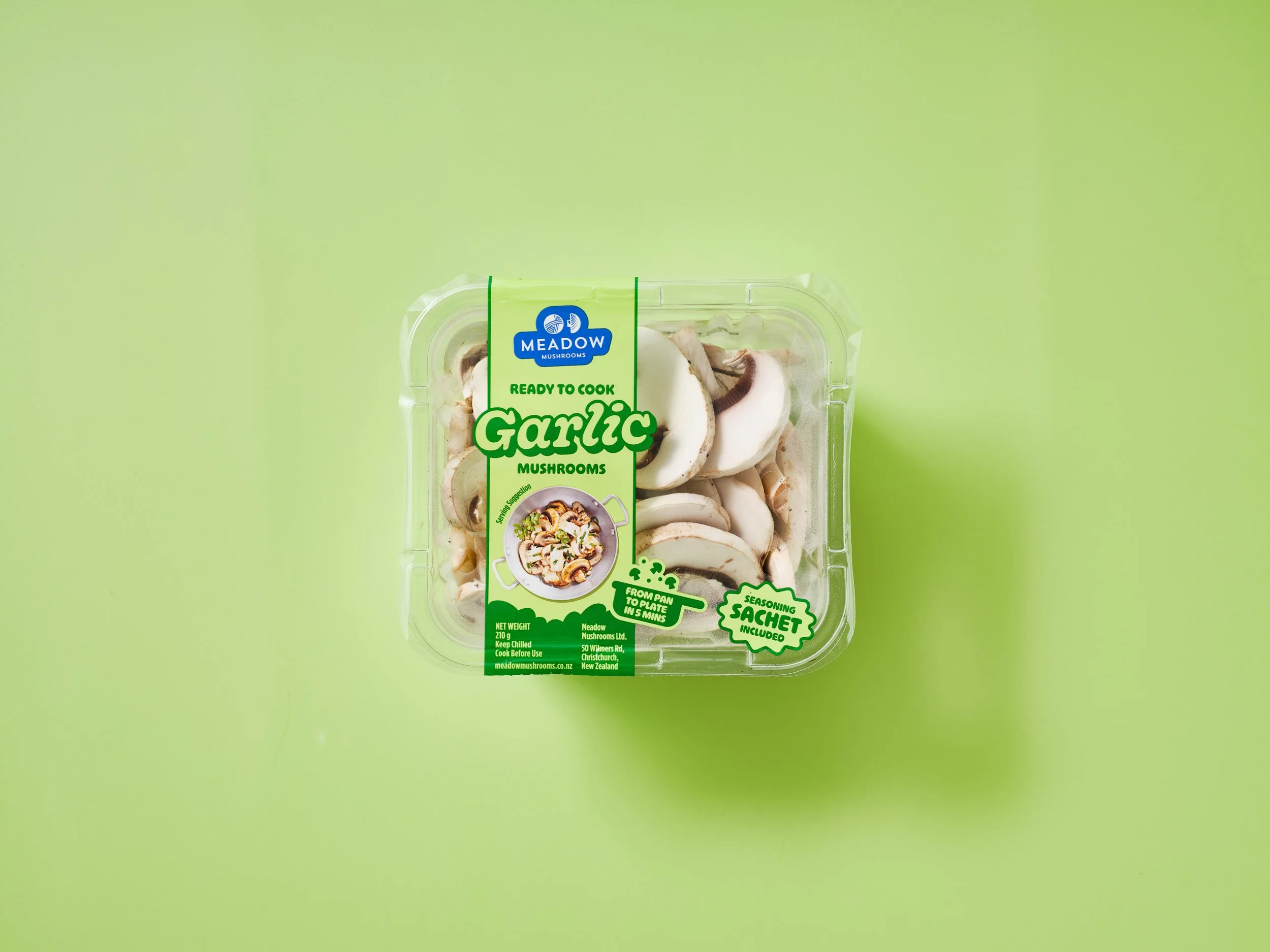 A package of meadow mushrooms labeled 'garlic' and 'ready to cook,' sitting on a green background.