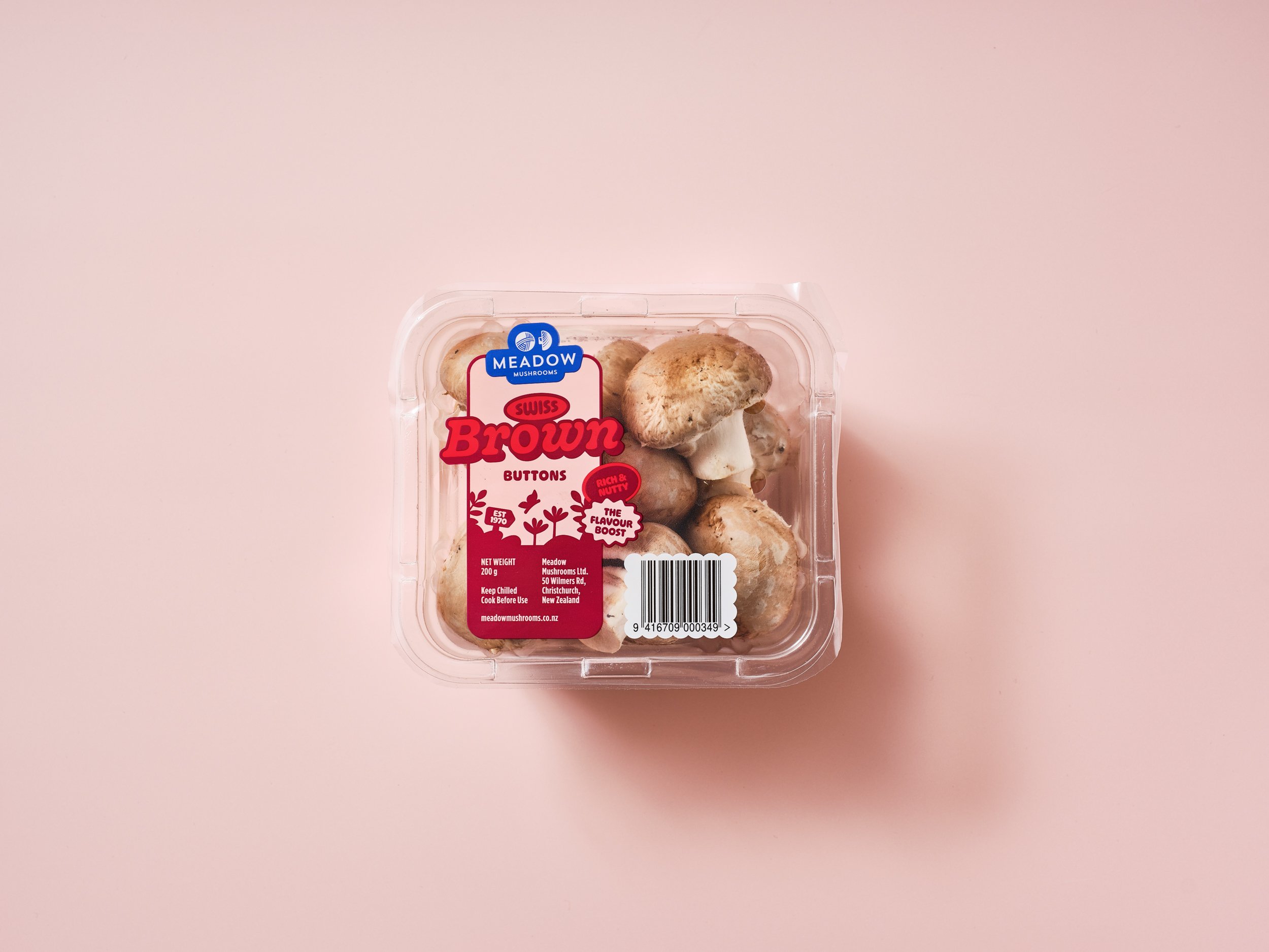 A plastic container of brown mushrooms labelled Meadow Mushrooms, placed on a pale pink surface.