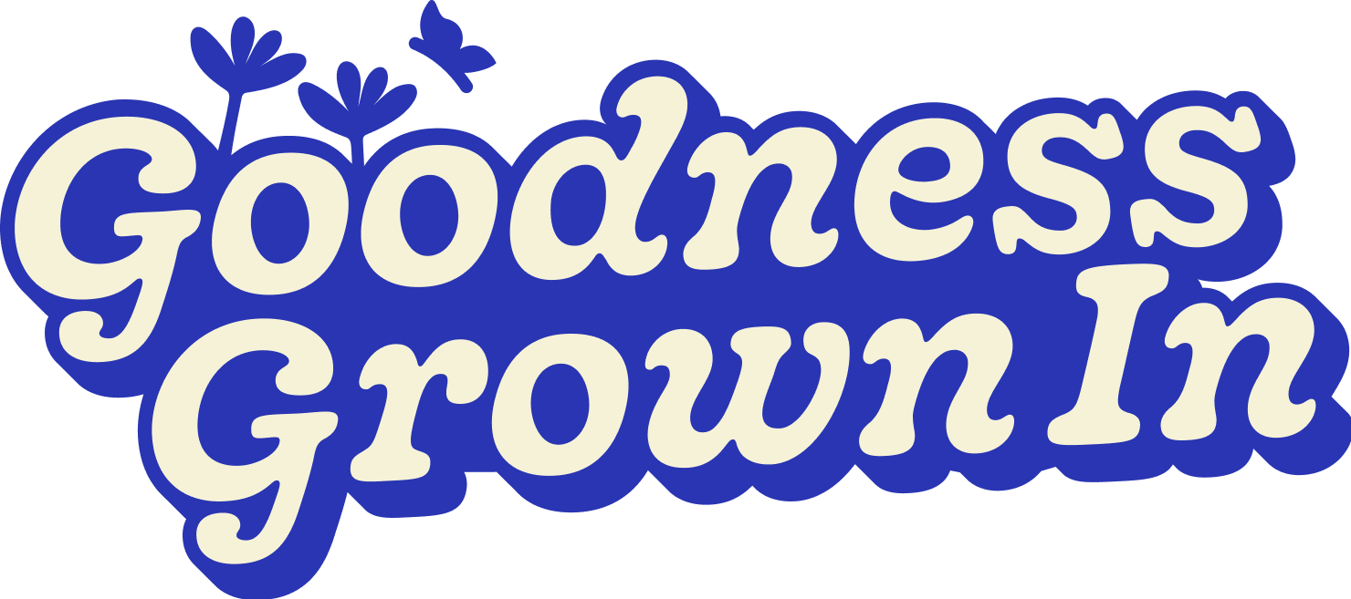 The words 'Goodness Grown In' written in large, playful, cream-colored font with a blue outline, accompanied by small, simple blue flowers and two blue butterflies.