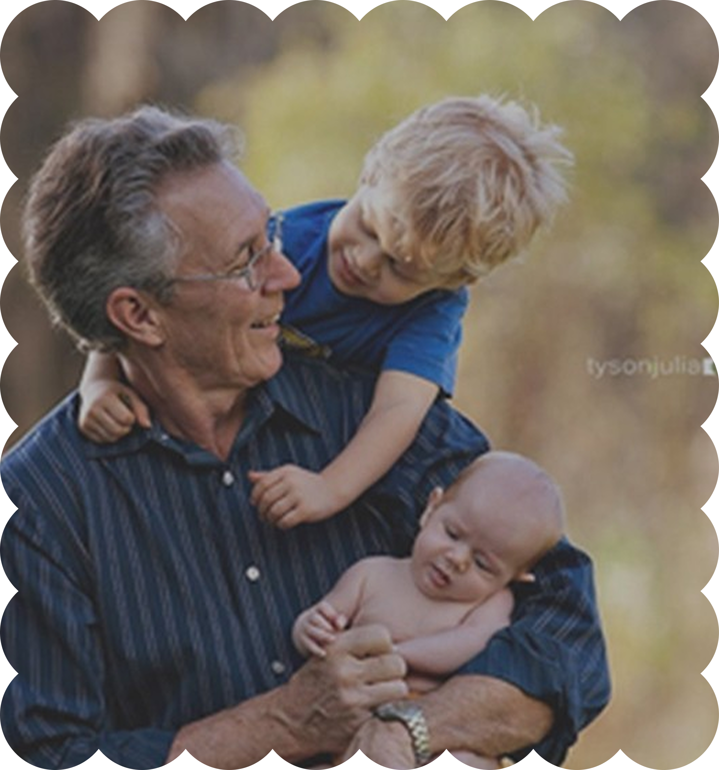 An elderly man with glasses and gray hair playing with two young children outdoors on a sunny day.