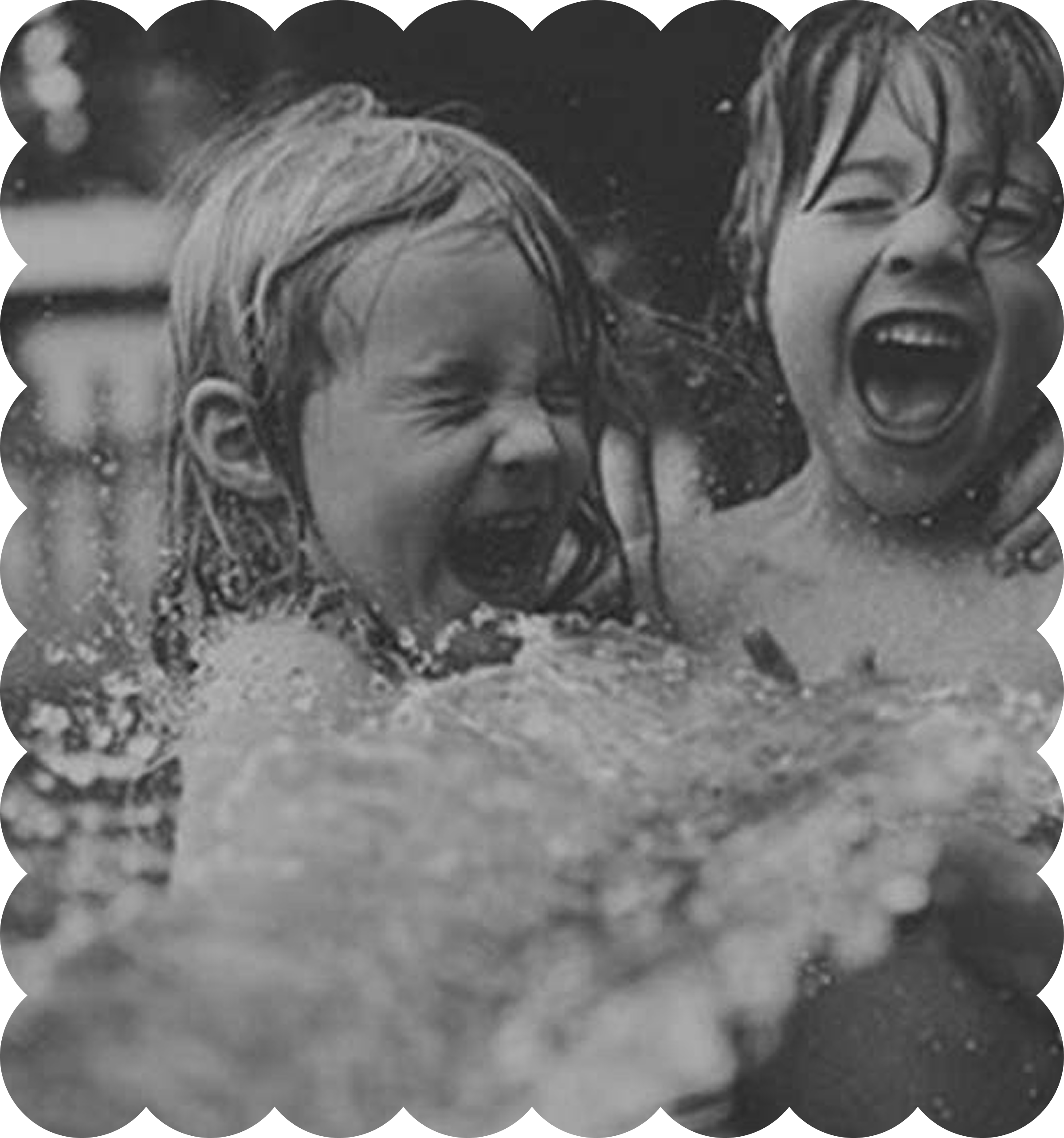 Black and white photograph of people joyfully enjoying a water activity, likely at a beach or pool.