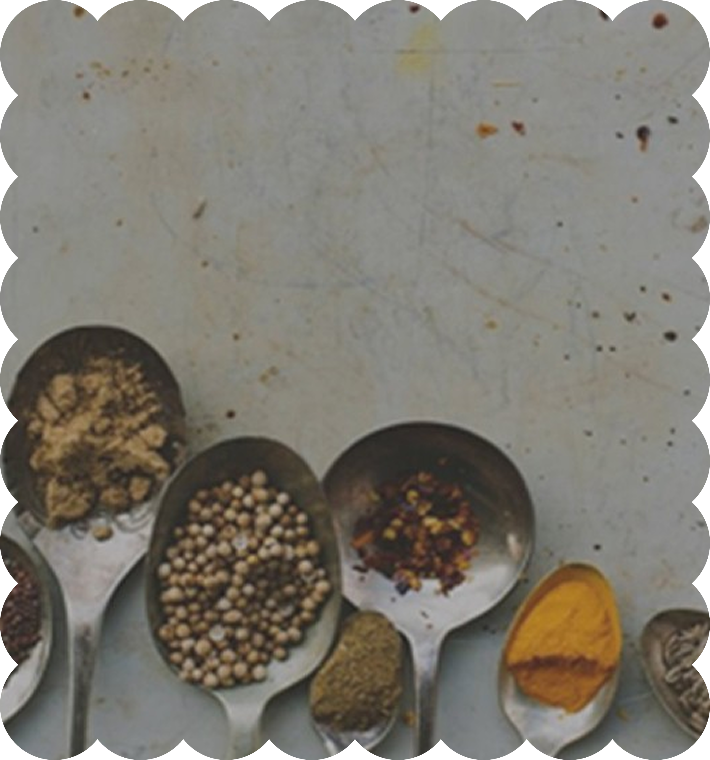 A variety of spices and herbs in small bowls on a white surface, including crushed red pepper, black peppercorns, garlic powder, turmeric, and other seasonings.