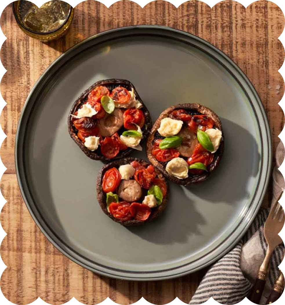 Three grilled portobello mushroom caps topped with cherry tomatoes, mozzarella cheese, basil leaves, on a gray plate.