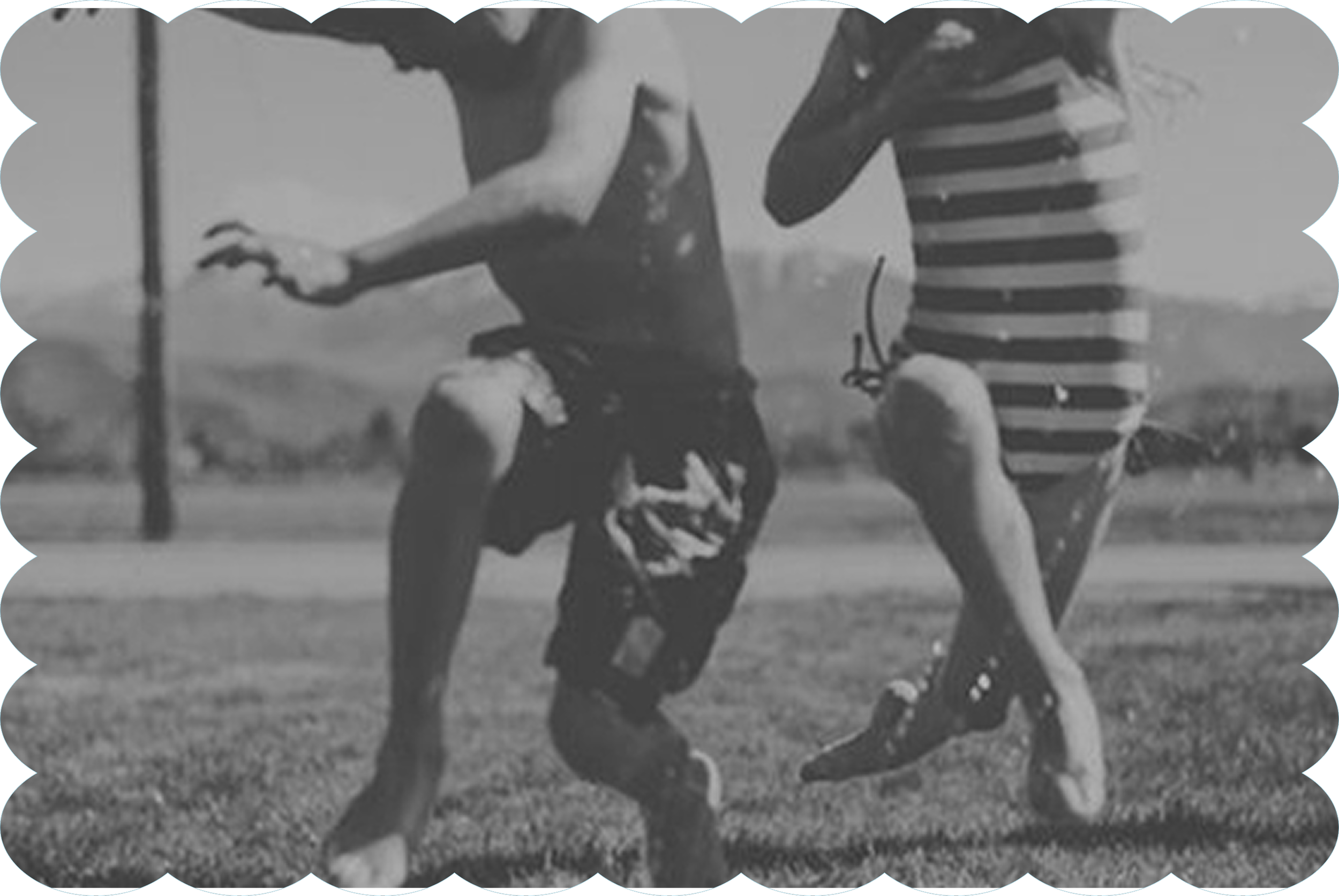 Two boys playing football outdoors, one is jumping to catch or intercept the ball while the other is reaching out with his hand. The background shows an open field with some trees or fences.