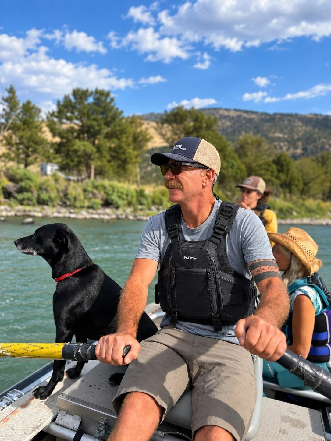 Two adults and two children on a boat in a river surrounded by trees and mountains under a partly cloudy sky.