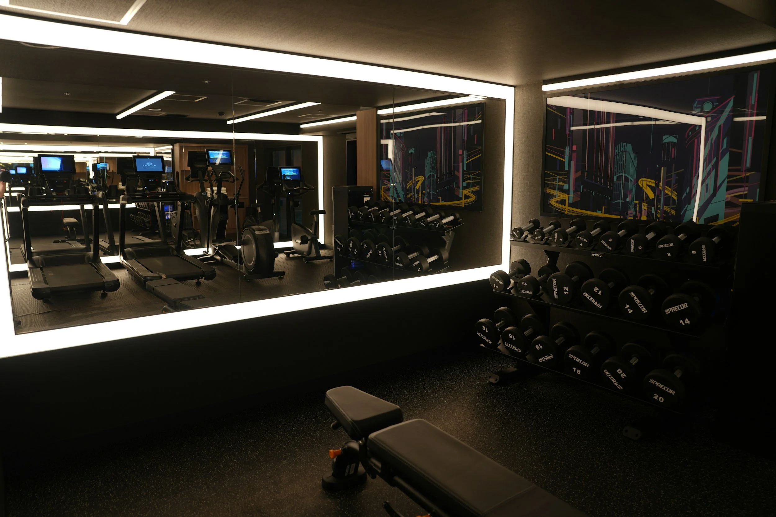 Interior of a modern gym with workout equipment including treadmills, stationary bikes, and dumbbells, with colorful abstract wall art.