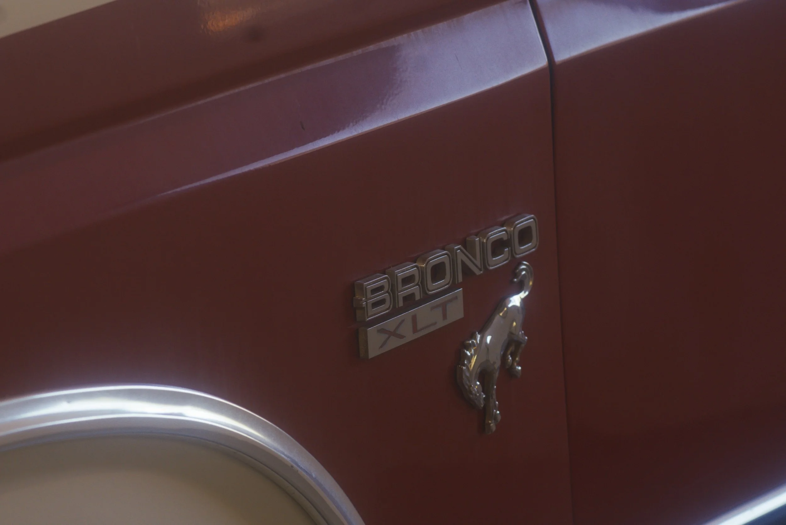 Close-up of a red vintage Bronco XL truck with silver emblem detailing.