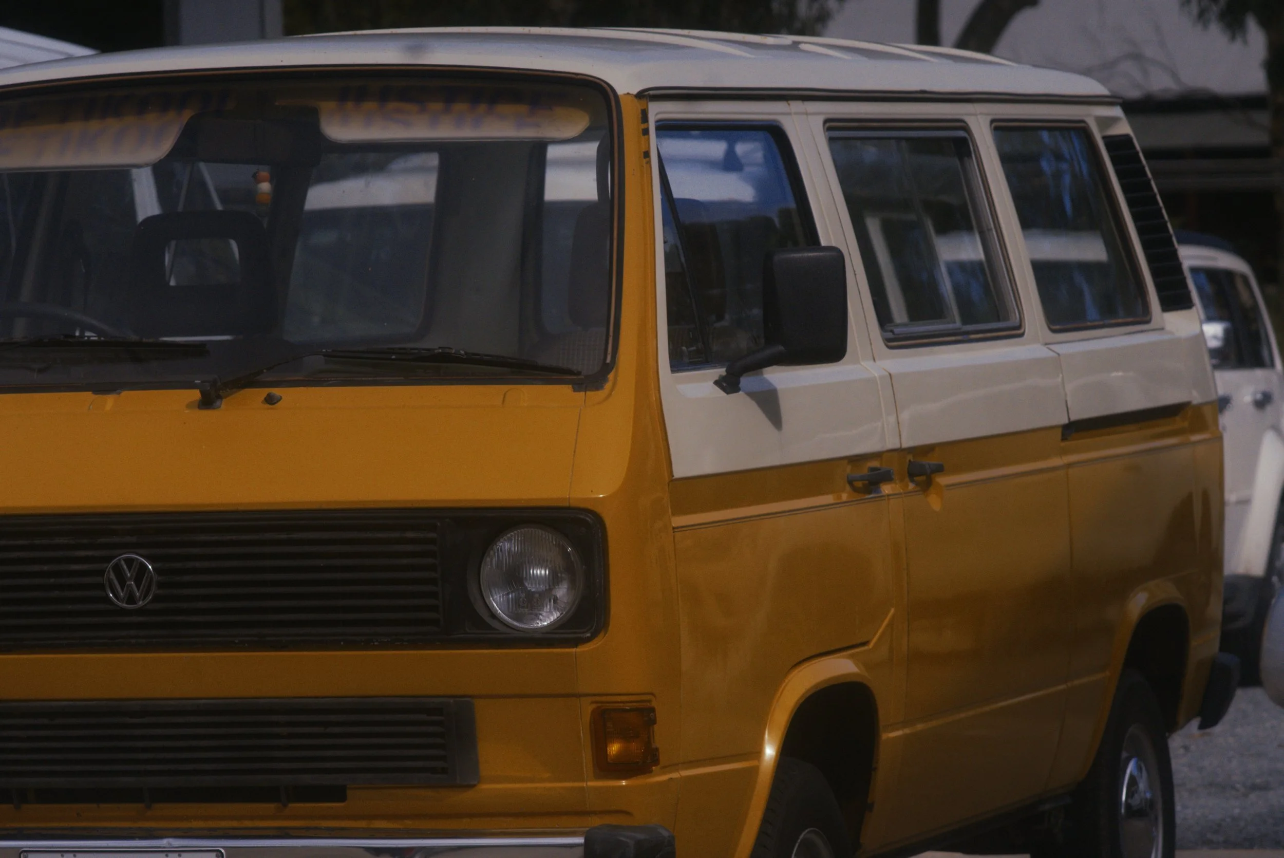 A yellow vintage Volkswagen van with a white upper section and black grille, parked outdoors during what appears to be late afternoon or evening.