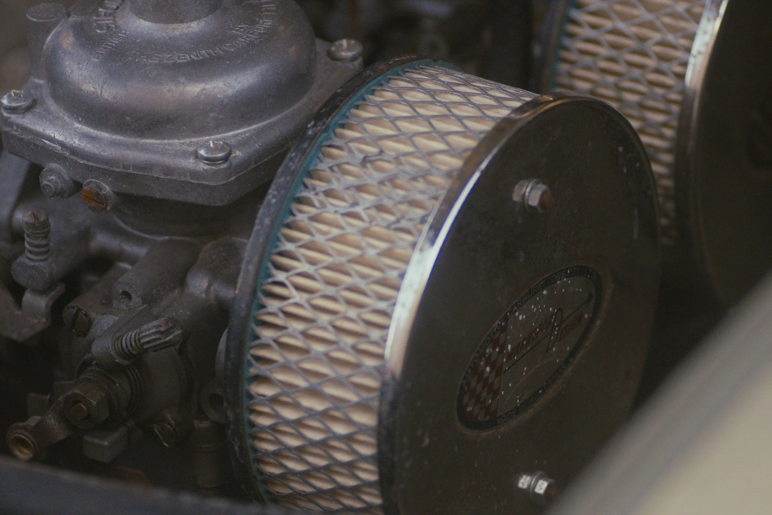 Close-up of a mechanical engine part with a cylindrical air filter with a diamond mesh pattern, attached to a metal engine component.