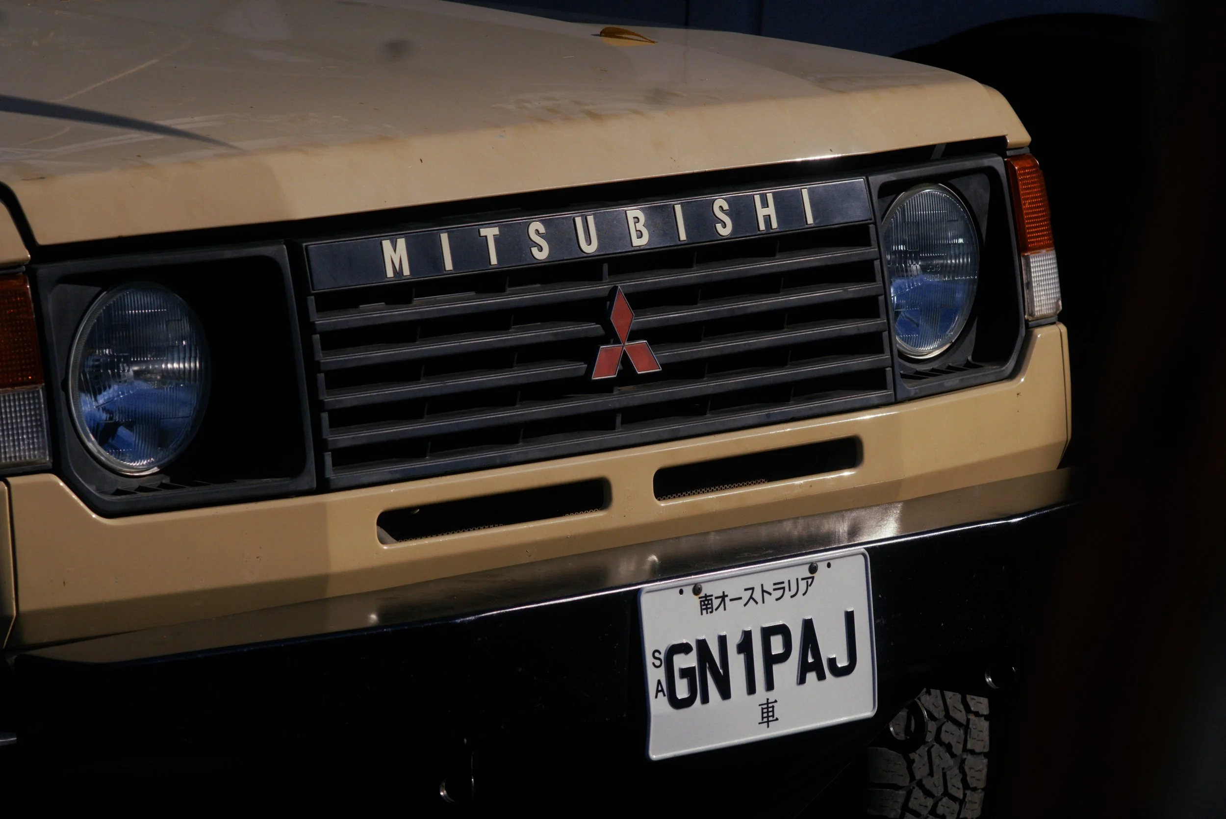 Front view of a beige Mitsubishi vehicle with a black grille, round headlights, and Japanese license plate.