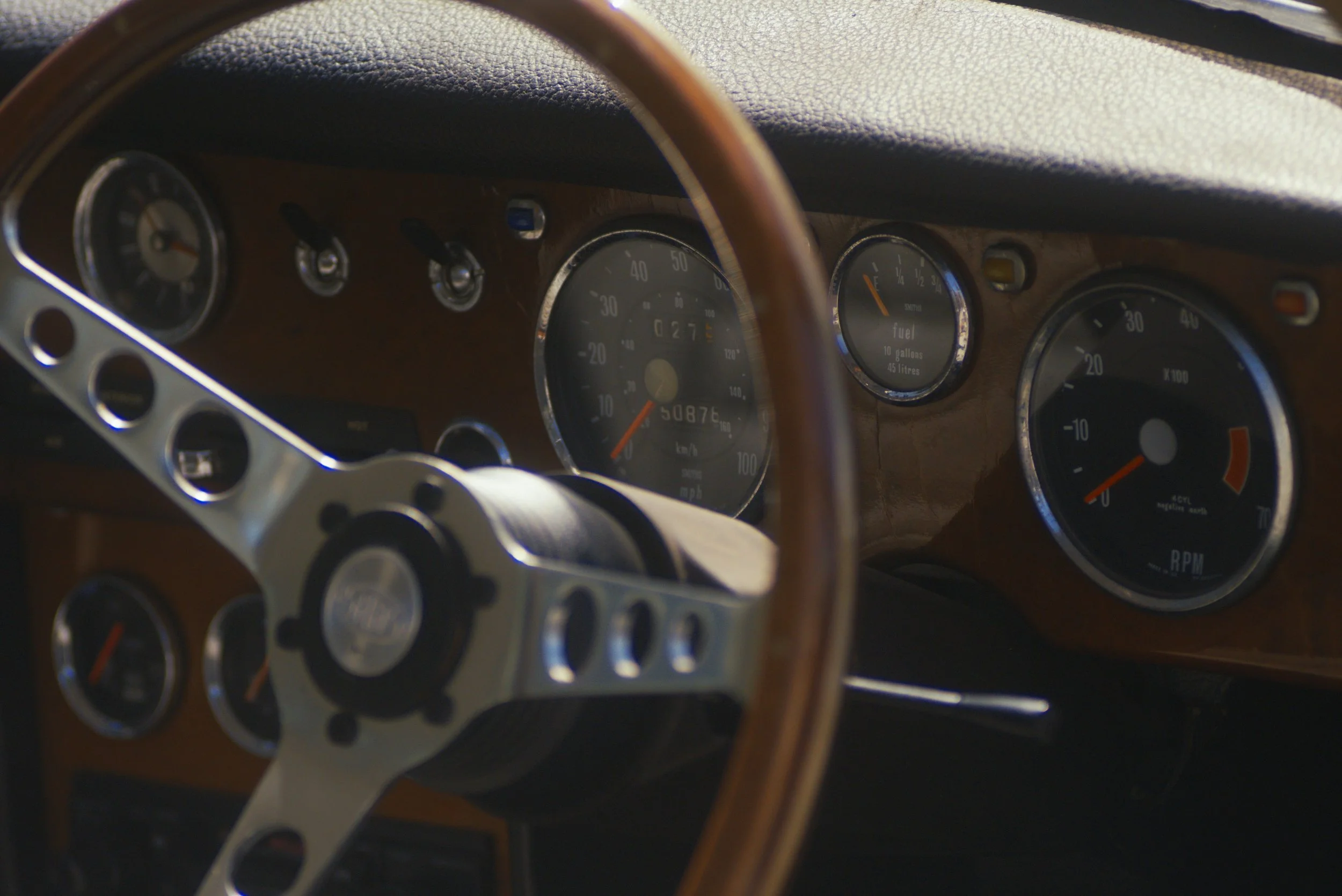 Close-up of a vintage car dashboard with gauges for speed, fuel, and RPM, and a wooden steering wheel.