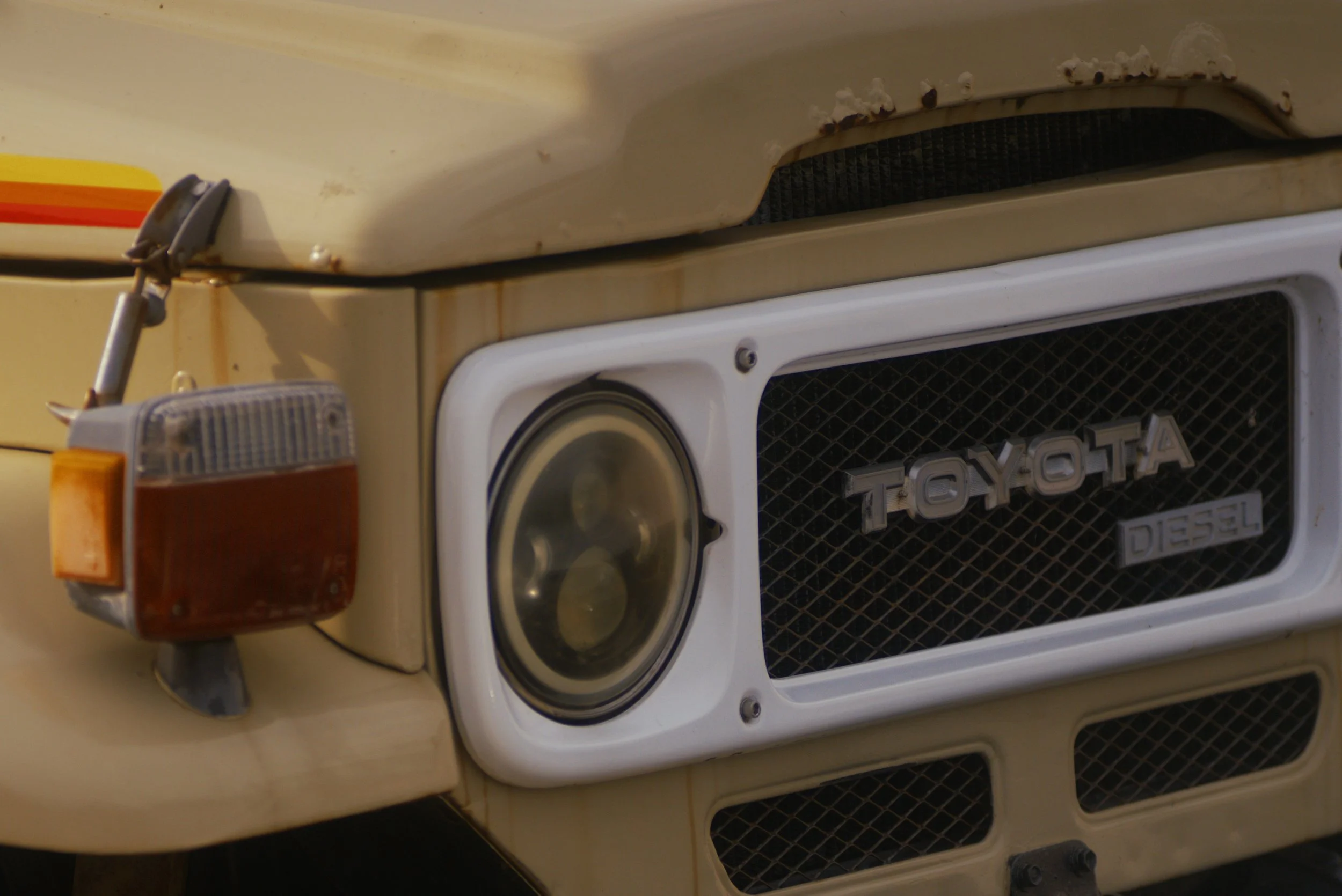 Close-up of the front of a beige Toyota Diesel vehicle with rust stains, showing the headlight, grille, and part of the hood.