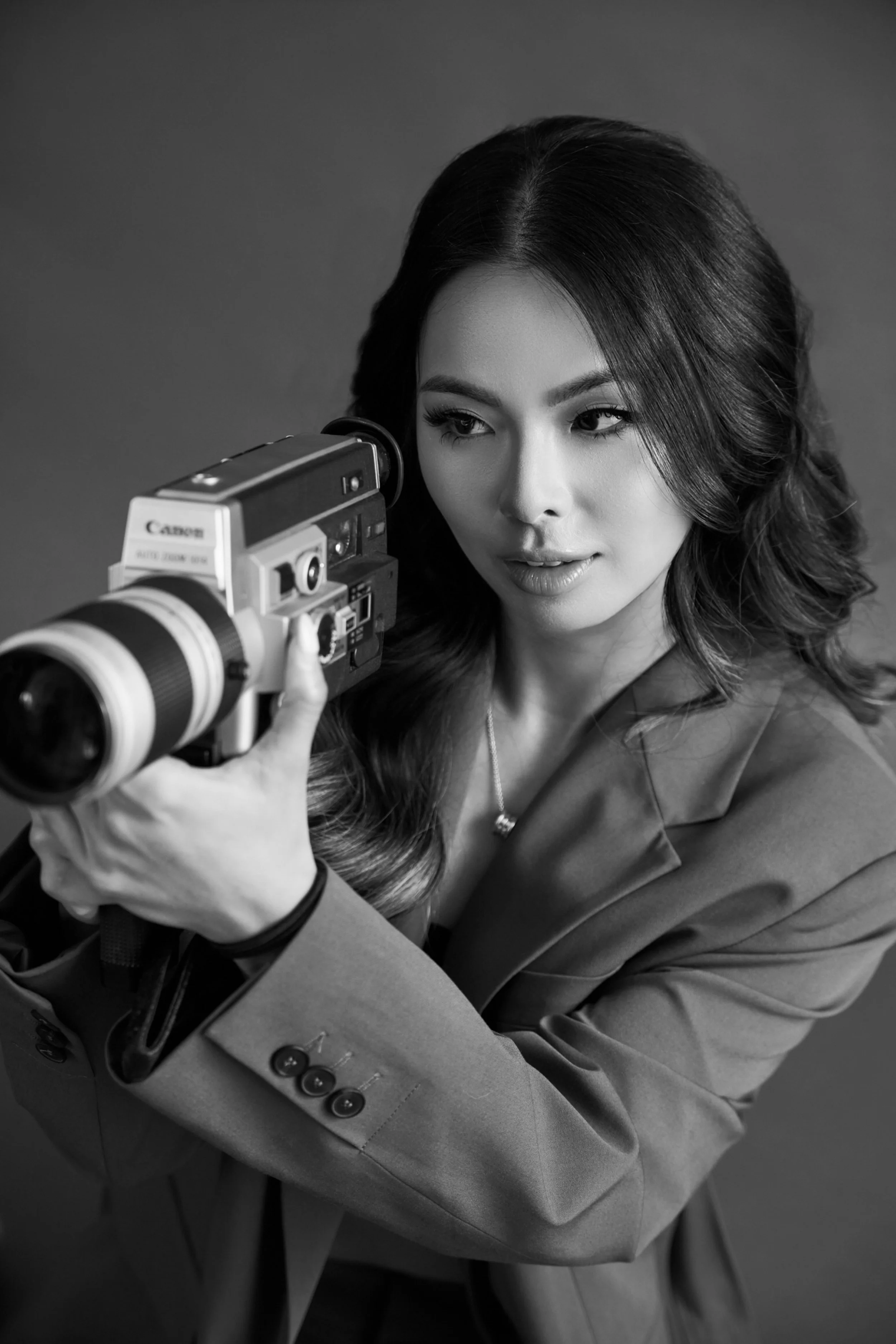 A wedding photographer in orange county los angeles with styled hair, wearing a blazer, looking through a professional camera with a large telephoto lens.