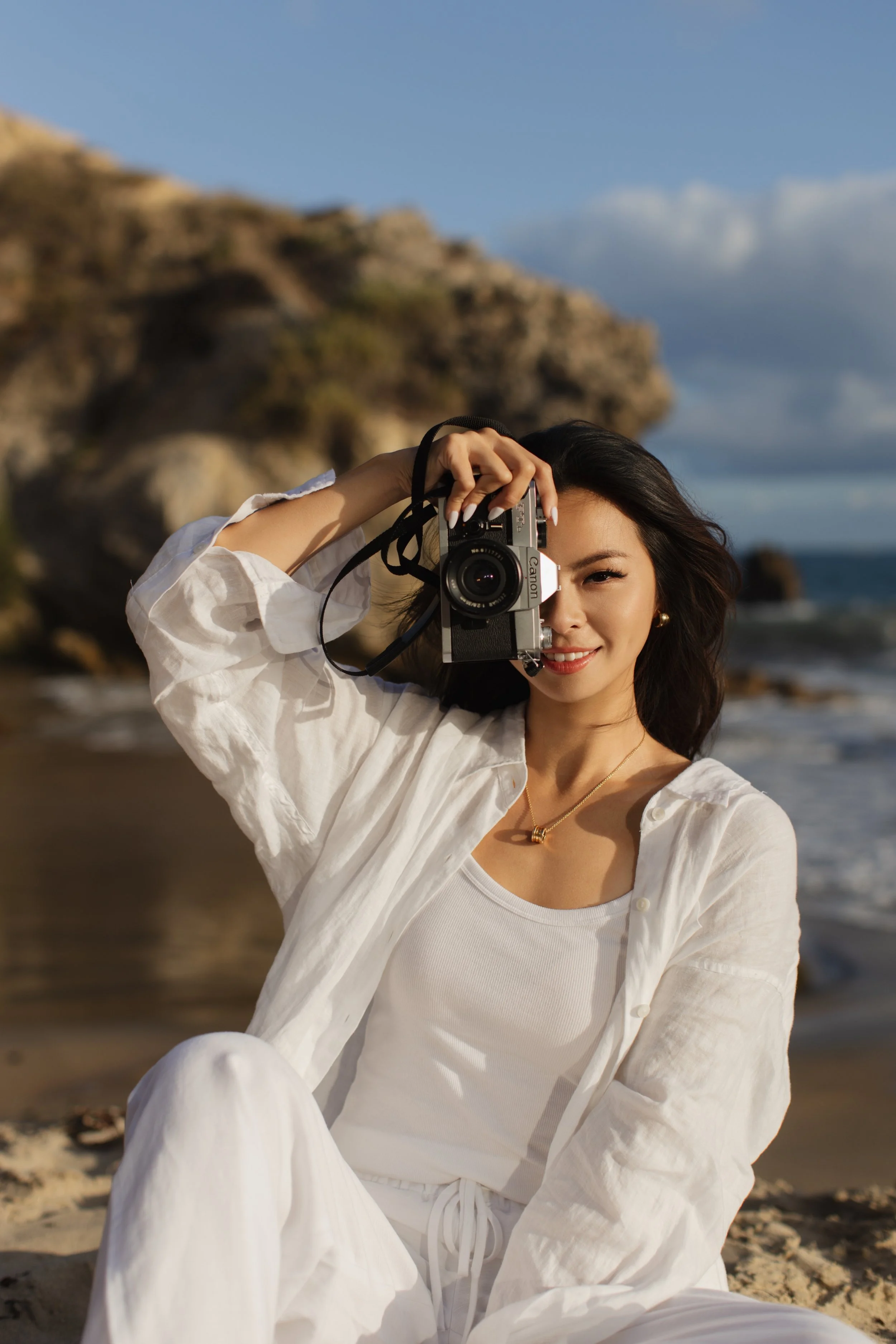South Asian wedding photographer Aishia at the beach holding a film camera