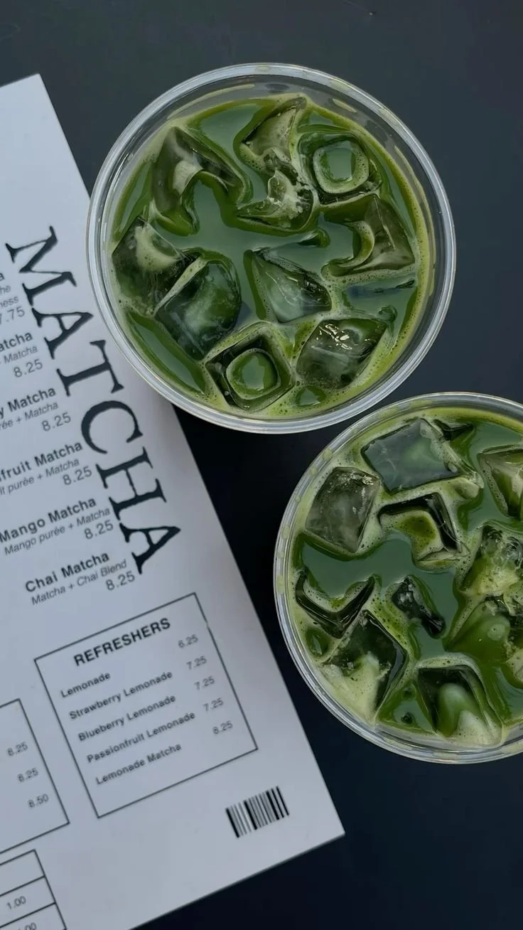 Two cups of iced matcha tea with ice cubes next to a menu at a cafe.