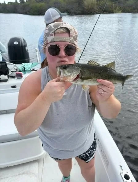 Woman holding a fish on a boat with water and trees in the background.