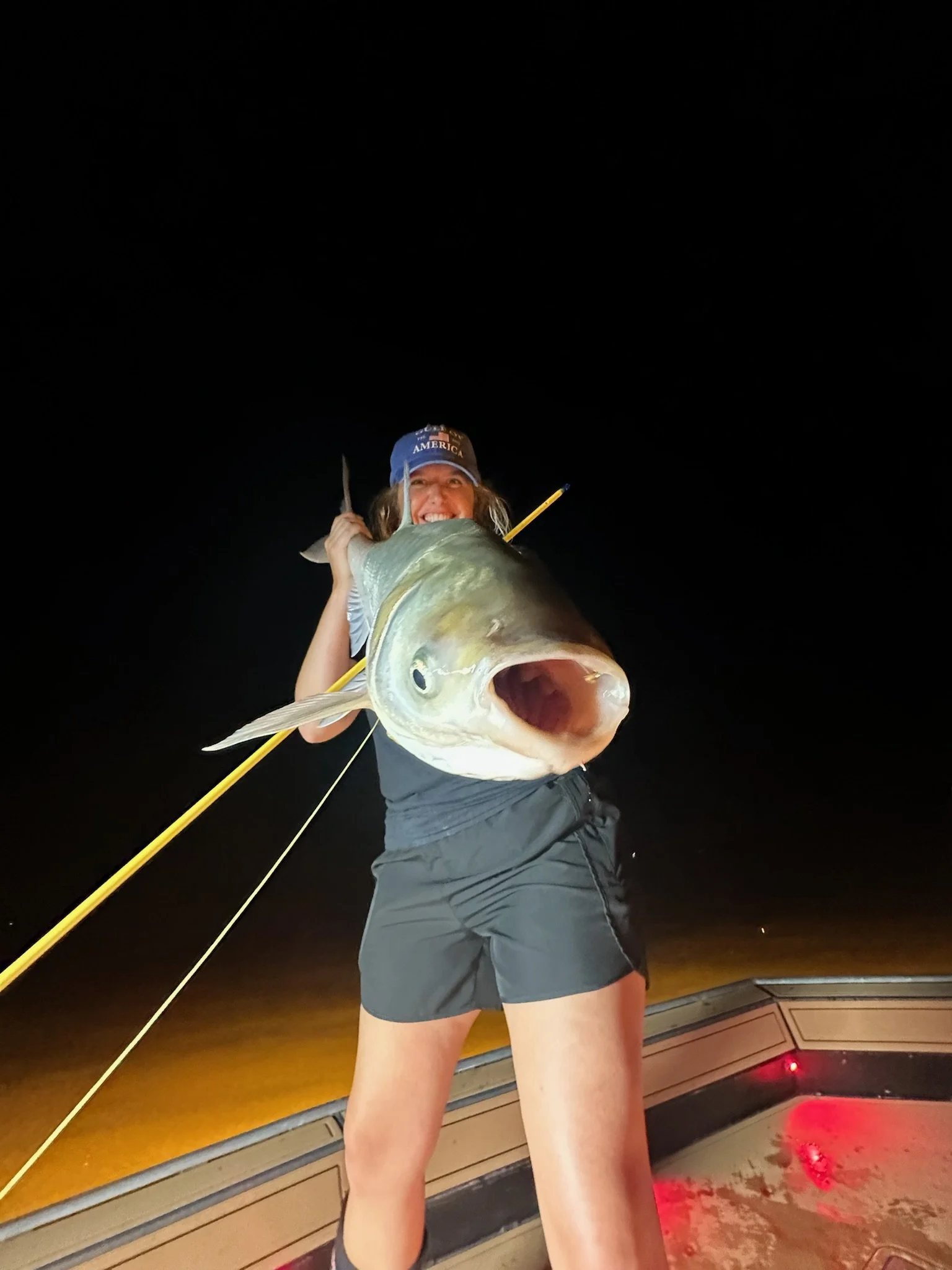 Person holding a large fish on a boat at night.