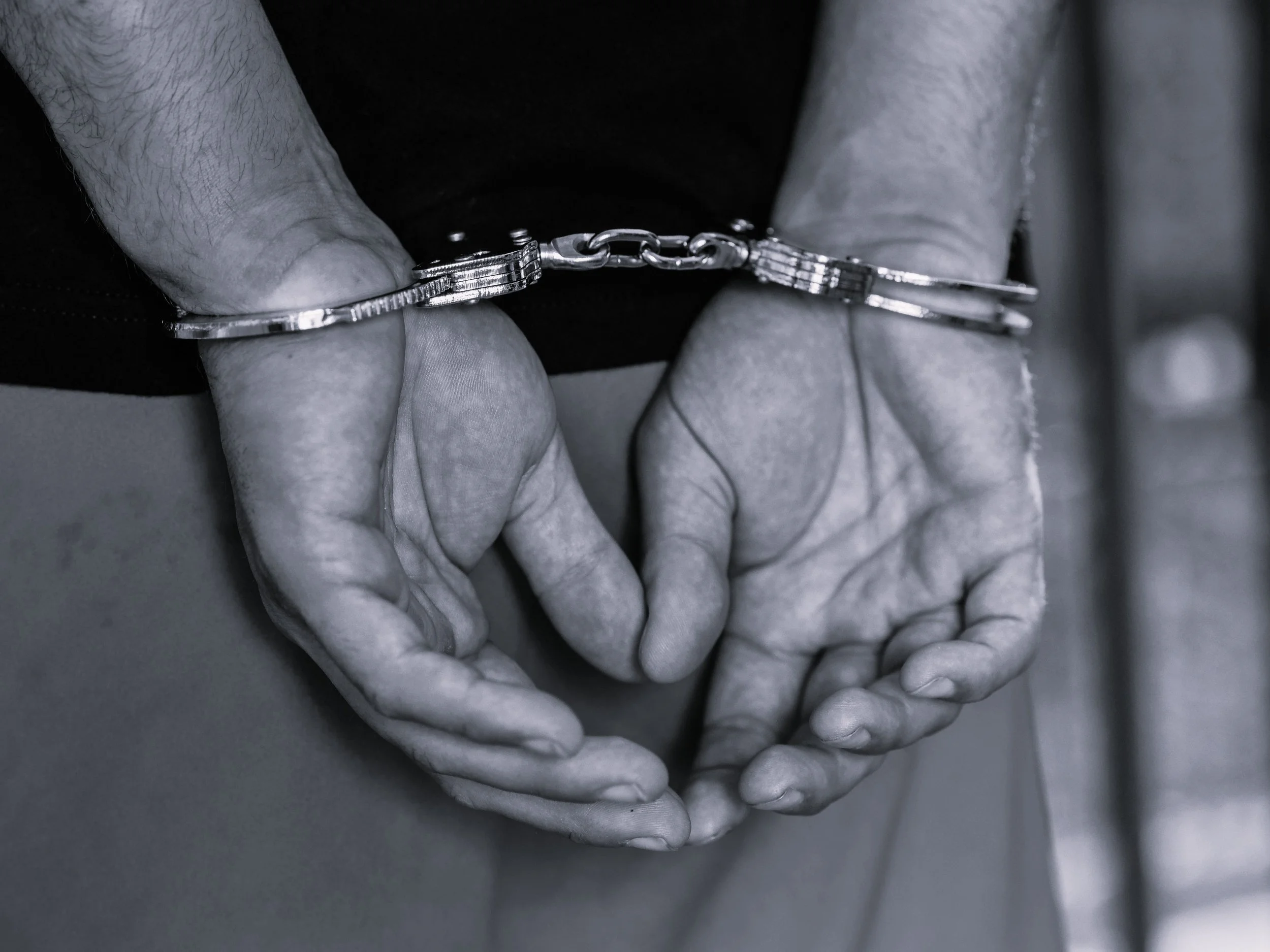 Close-up of hands connected by a chain, with fingers gently touching at the tips, in black and white.