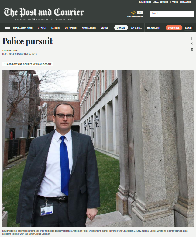 A man in a suit and blue tie standing outside near a brick building and stone columns.
