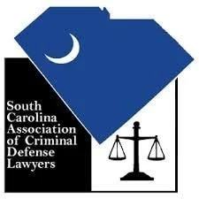 Logo of the South Carolina Association of Criminal Defense Lawyers featuring a stylized shield, a crescent moon, and a balanced scale of justice.