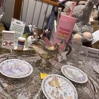 Decorative plates with floral designs on a table with various items including a pink donation jar, a small cake, and other party supplies.
