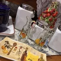 Tray with assorted small bottles, glasses, and a bowl of strawberries on a table.