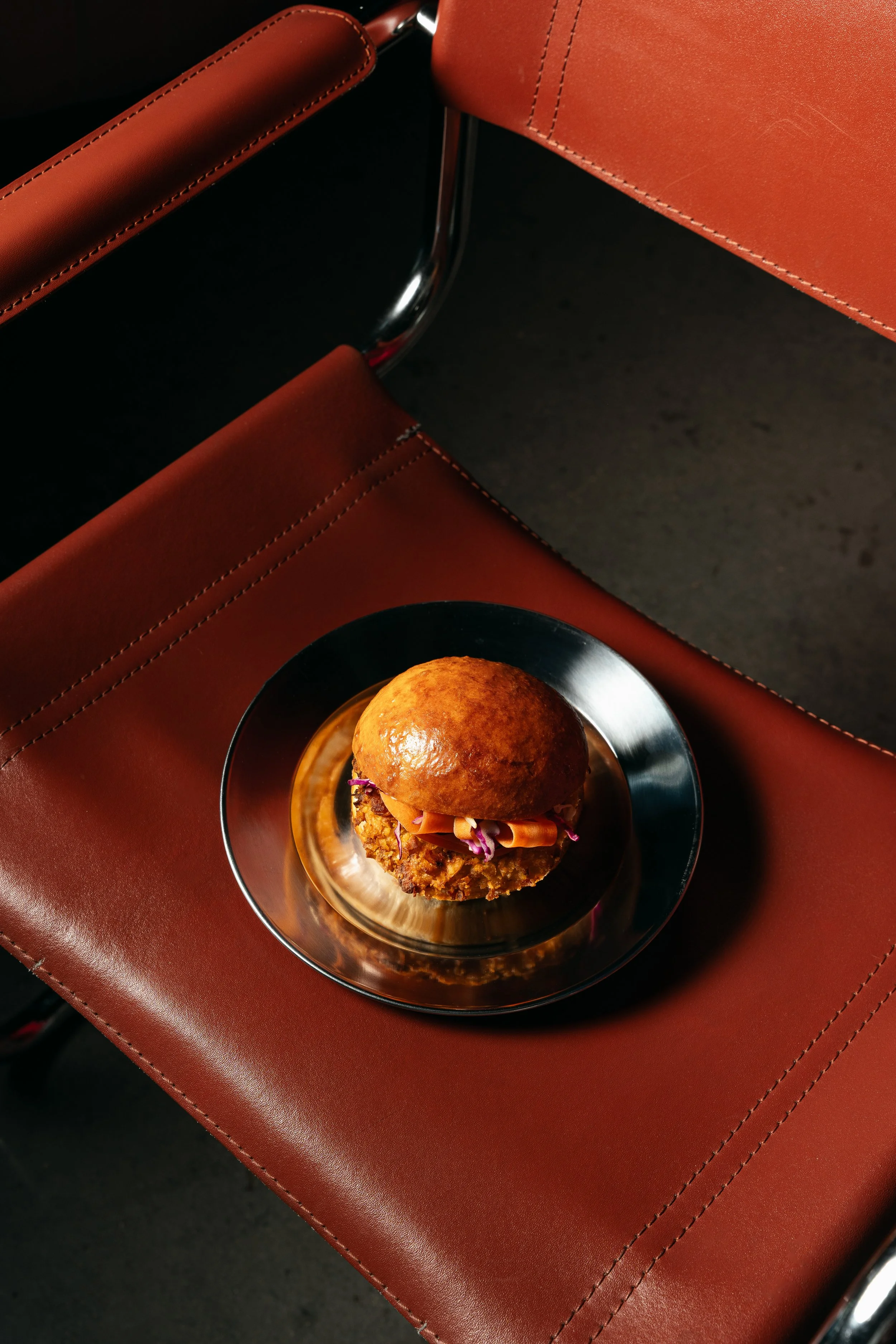 Hamburguesa en un plato de metal sobre una mesa de color marrón oscuro, con un fondo negro.