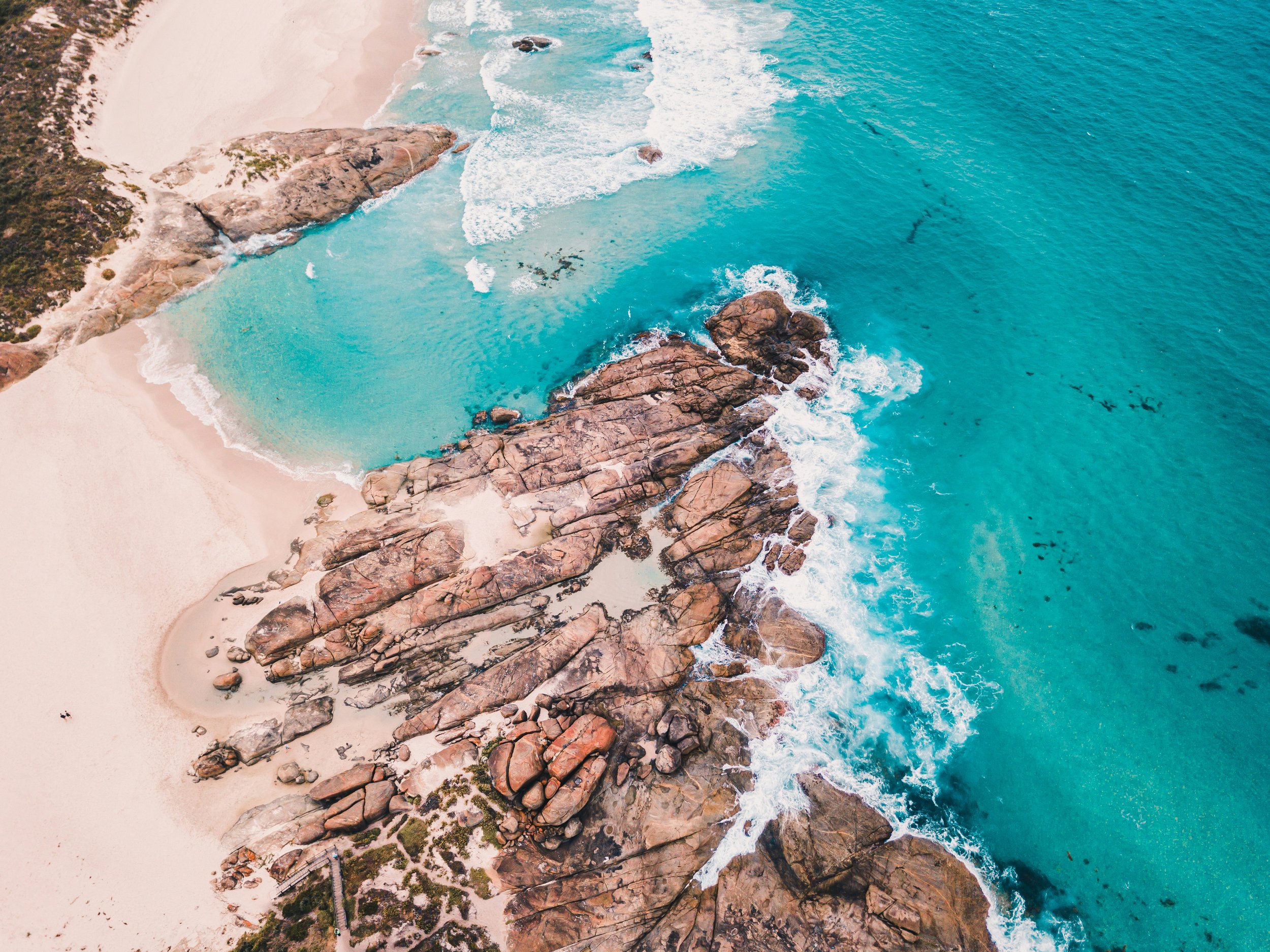 An aerial view of a beach with white sand, large rocks, and turquoise ocean waves.