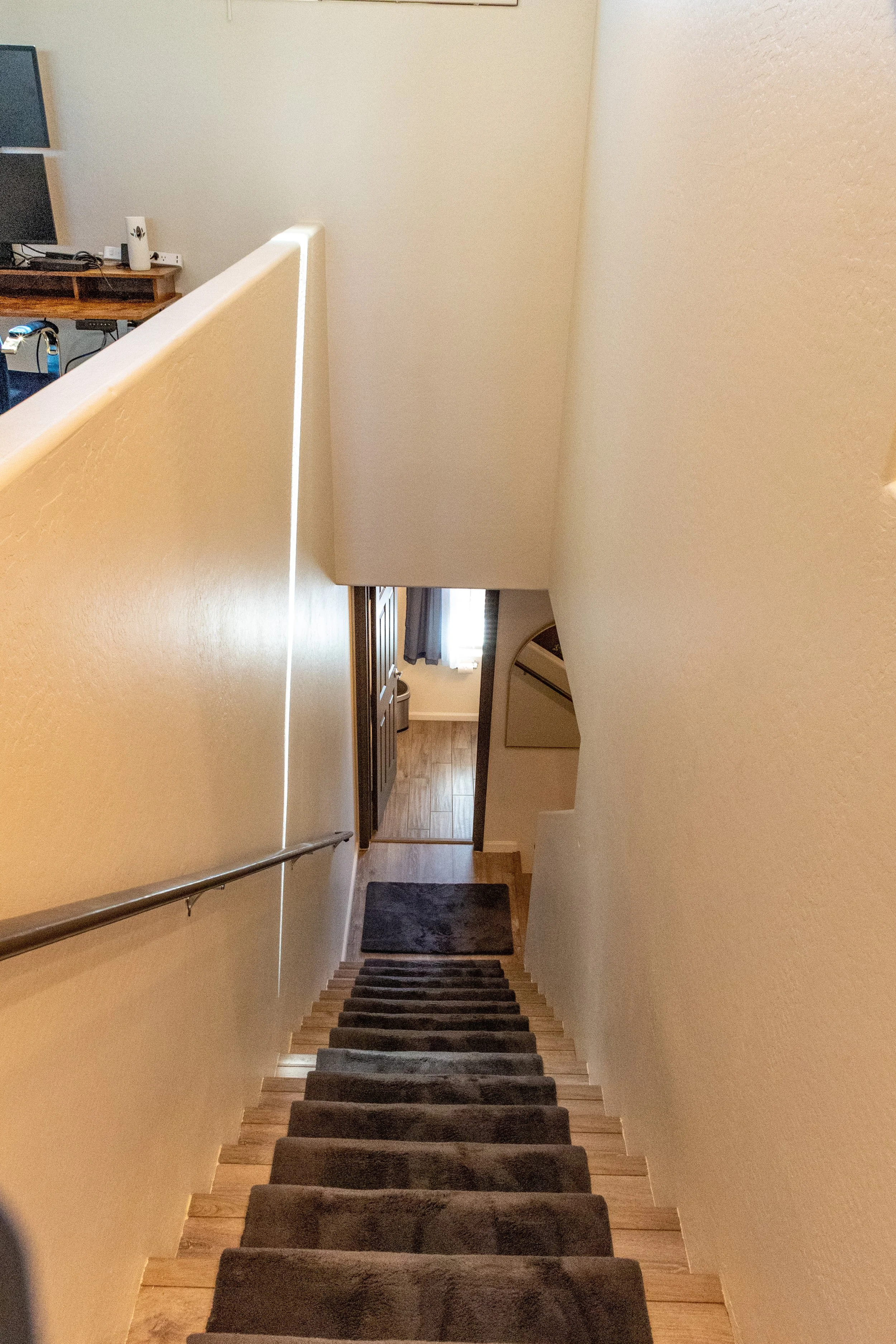 A staircase with dark carpeted steps leading down to a small entryway, with a curtain-covered window and a wooden door.