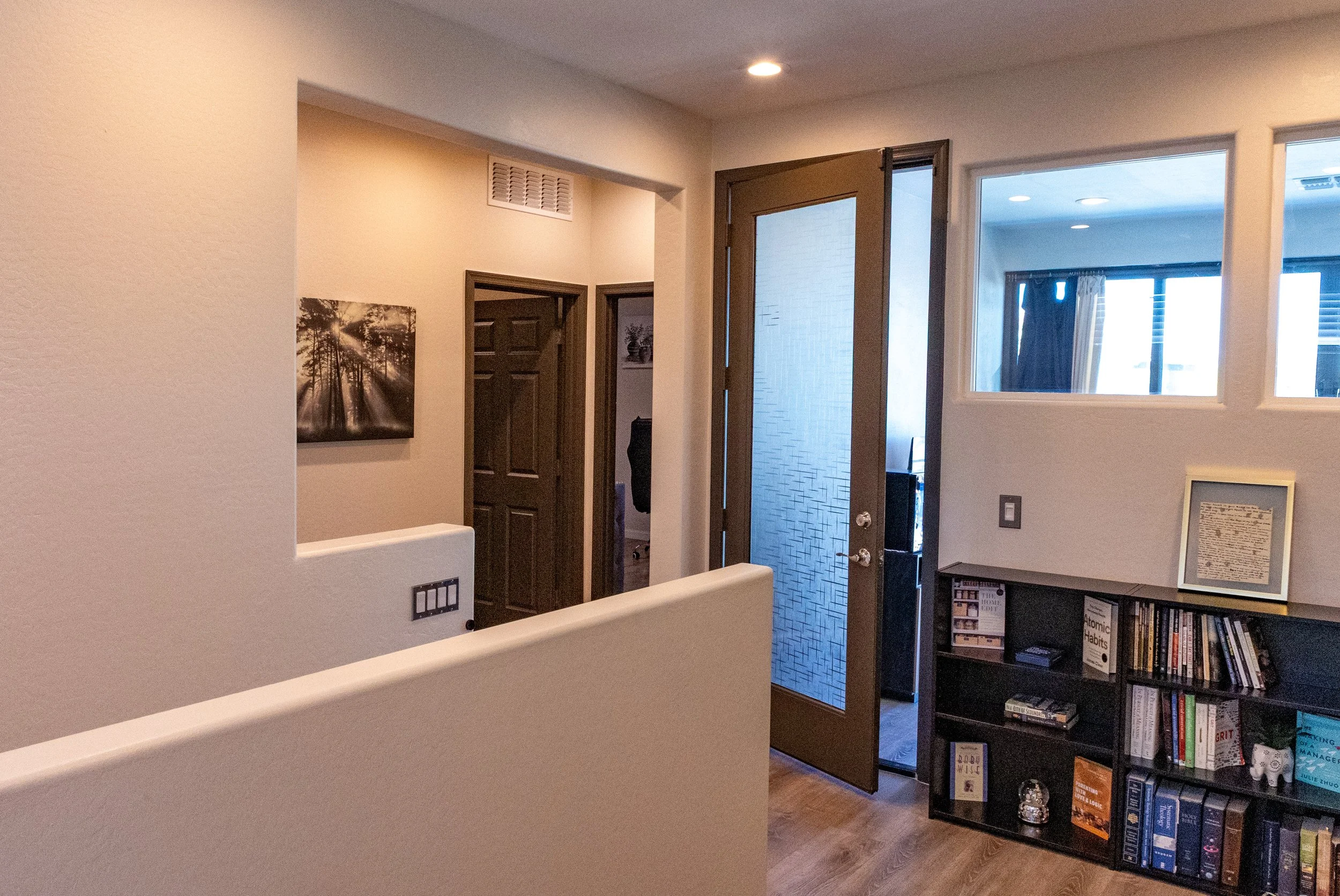 Interior view of a home entryway with a open main door, a bookshelf filled with books, and a framed picture on a table. There are two closed doors and two windows visible.