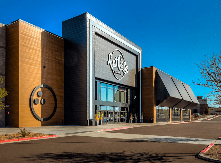 Exterior of a modern shopping mall with a large 'Fatty's' sign, featuring glass, wood, and metal architecture under a clear blue sky.