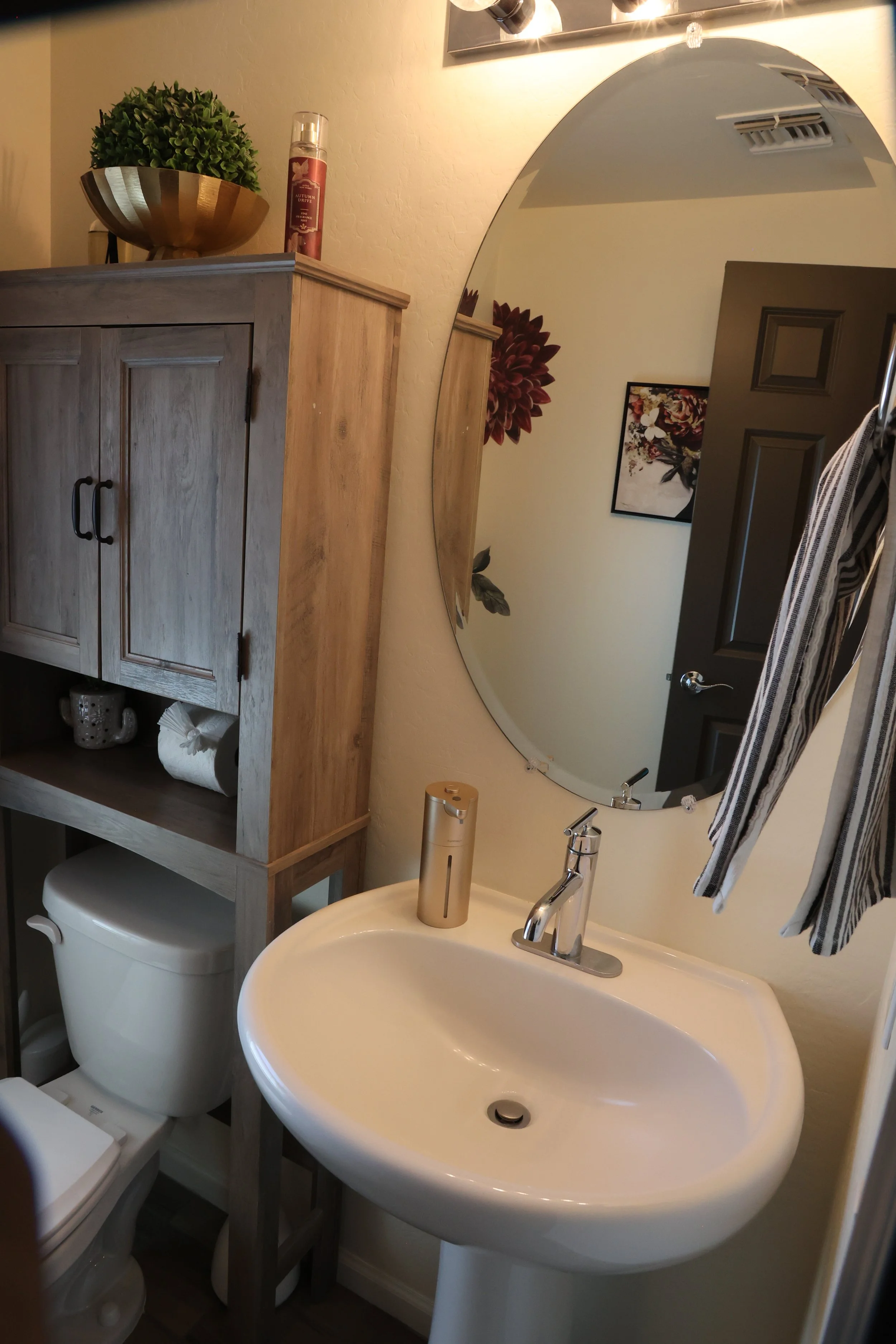 A bathroom with a white sink, mirror, wooden cabinet, toilet, and various toiletries and decorations.