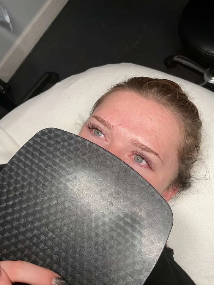 A woman lying on an examination table, partially covered by a black textured sheet, with her face visible and looking up, in a clinical setting.