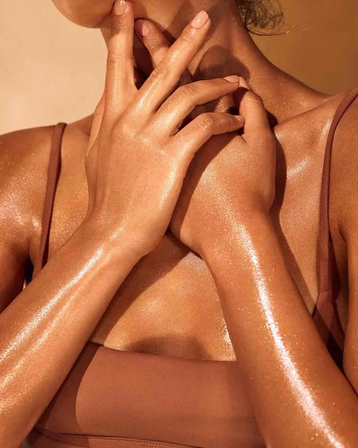 Close-up of a woman's hands and shoulders, with shiny, dewy skin, wearing a tan tank top.