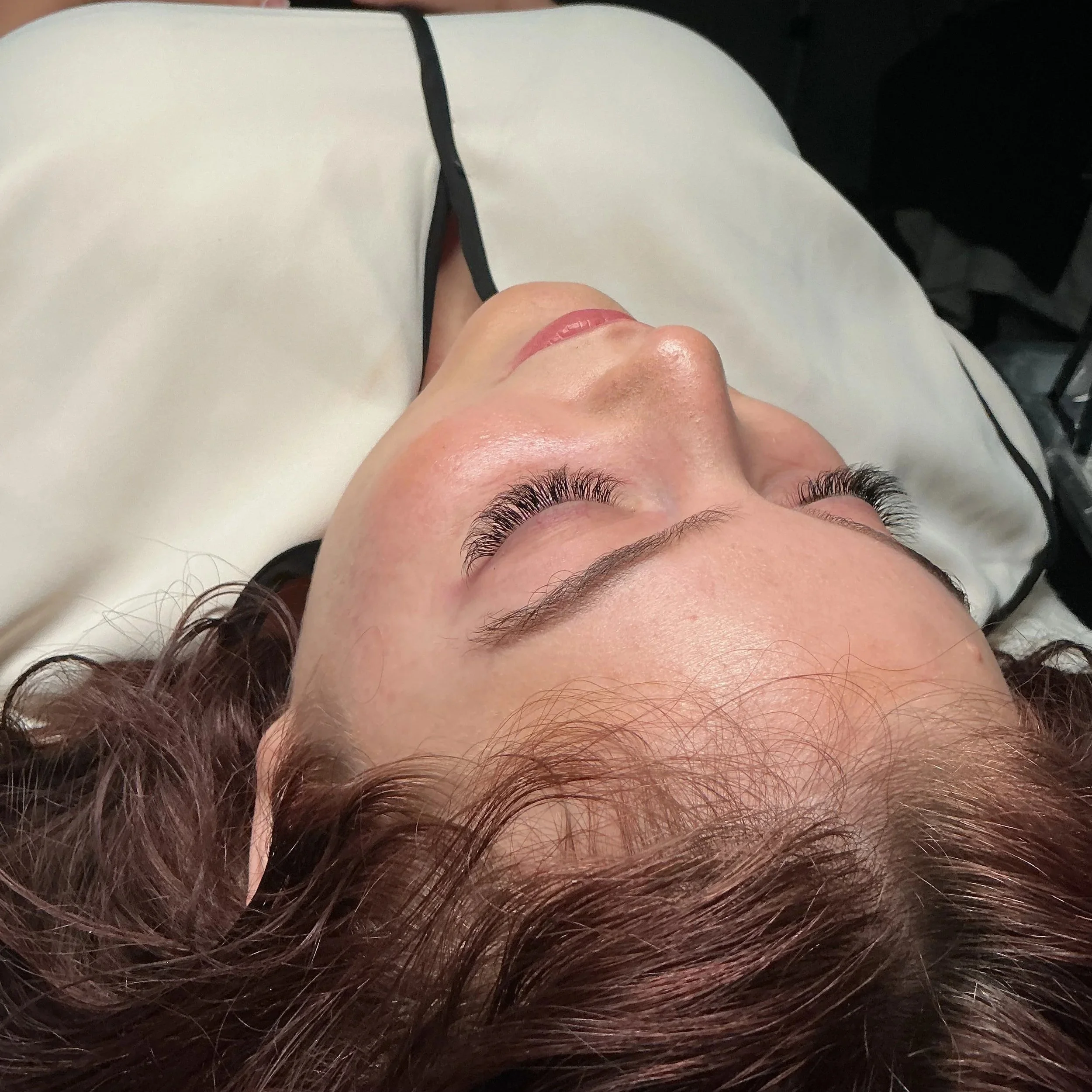 Close-up of a person's face and curly hair, lying on a white surface with a black strap visible across the face.