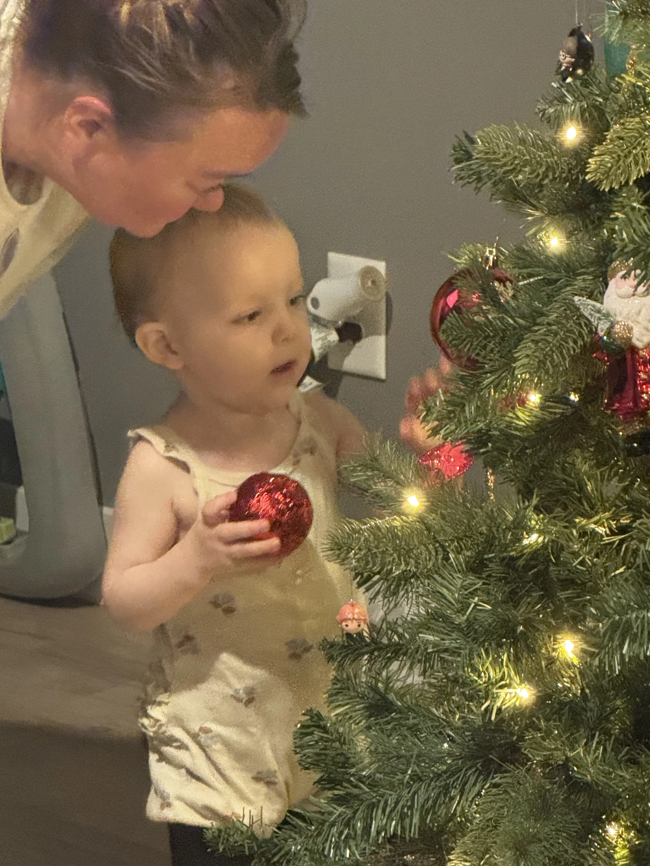 A woman and a young girl decorating a Christmas tree with ornaments and lights.