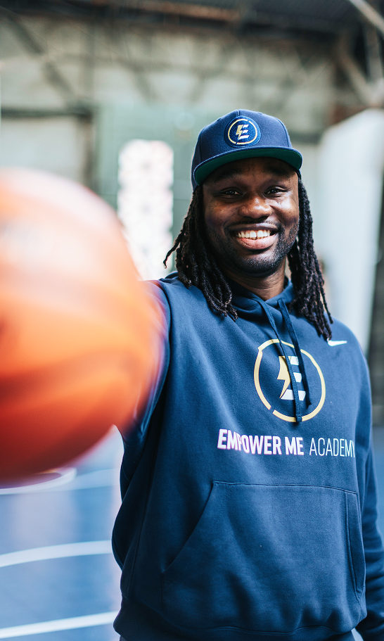 Coach Jerome Gumbs Smiling on a basketball court, with a basketball in his hand