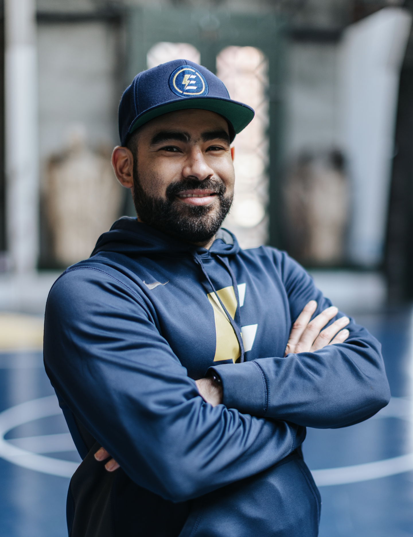 Coach Andrew smiling with arms crossed, in an outdoor area with architectural structures in the background.