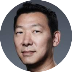 Close-up of an Asian man with short black hair, looking directly at the camera, neutral expression, plain dark background.
