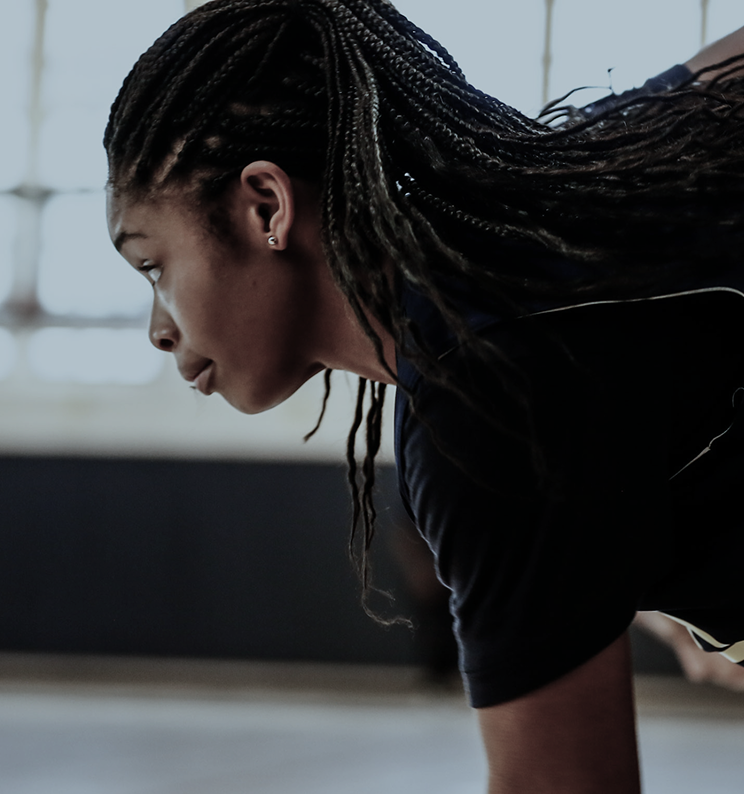 A woman with braided hair doing a physical exercise indoors.