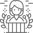 Simple line drawing of a person with a crown or diadem, surrounded by sparkles, behind a desk or podium.
