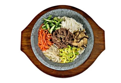 A bowl of assorted vegetables and sliced beef on a wooden serving board.